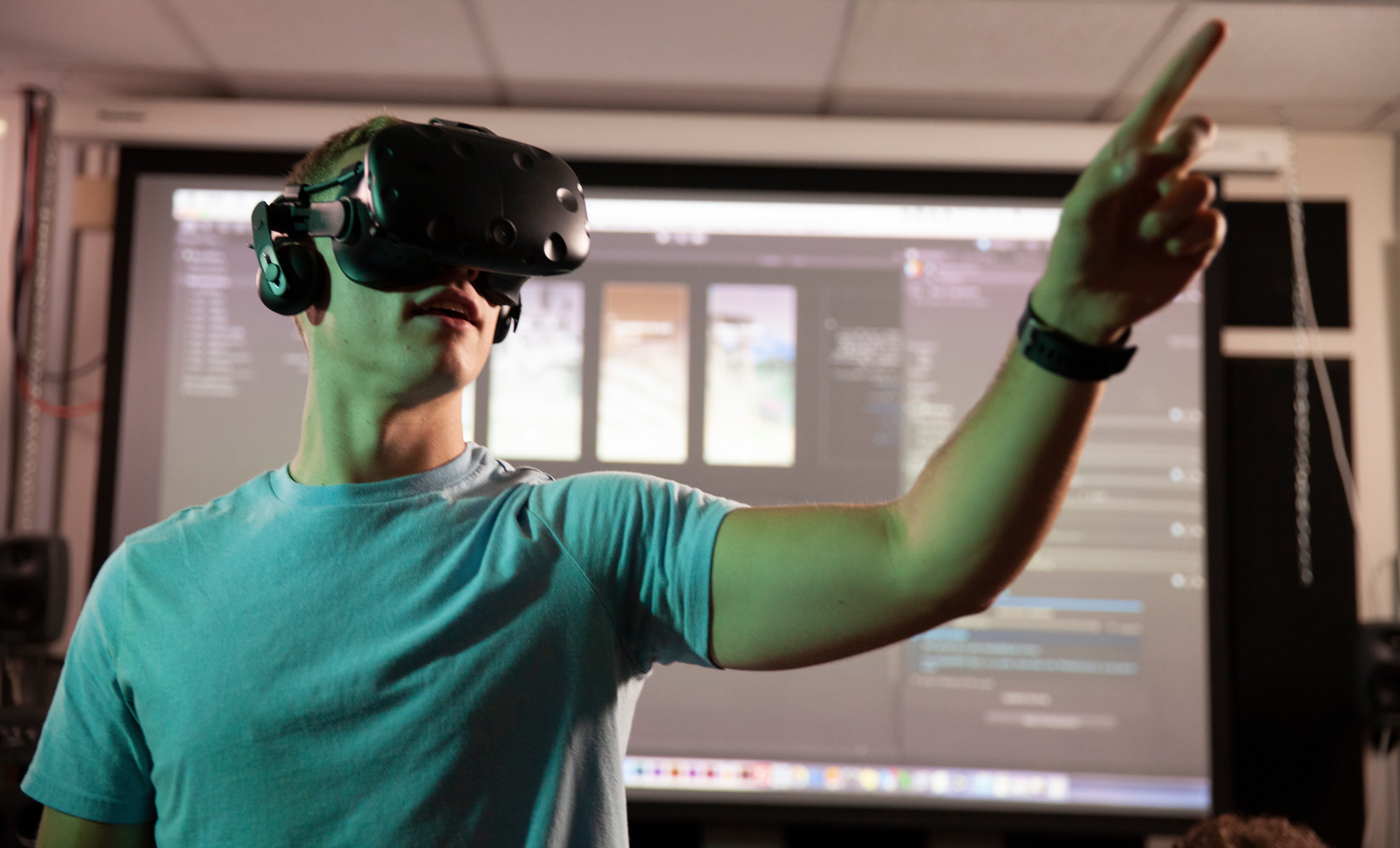 Man with grey shirt wearing a virtual reality headset pointing to the right