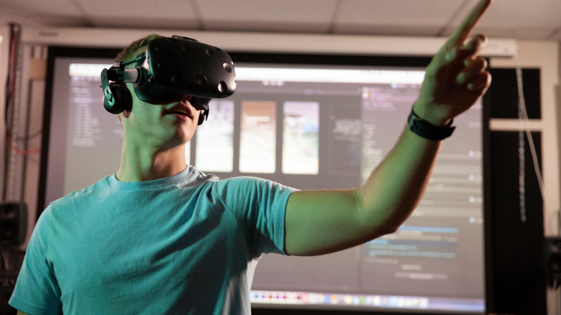 Man with grey shirt wearing a virtual reality headset pointing to the right