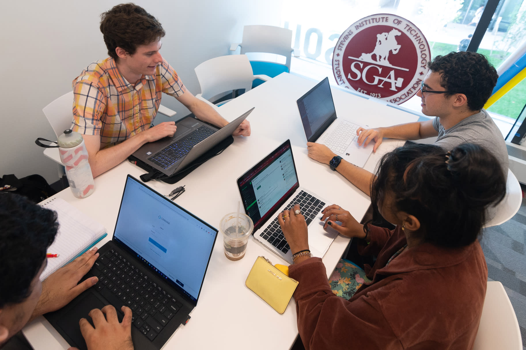 Students gathered around table on their laptops with SGA sign behind them.