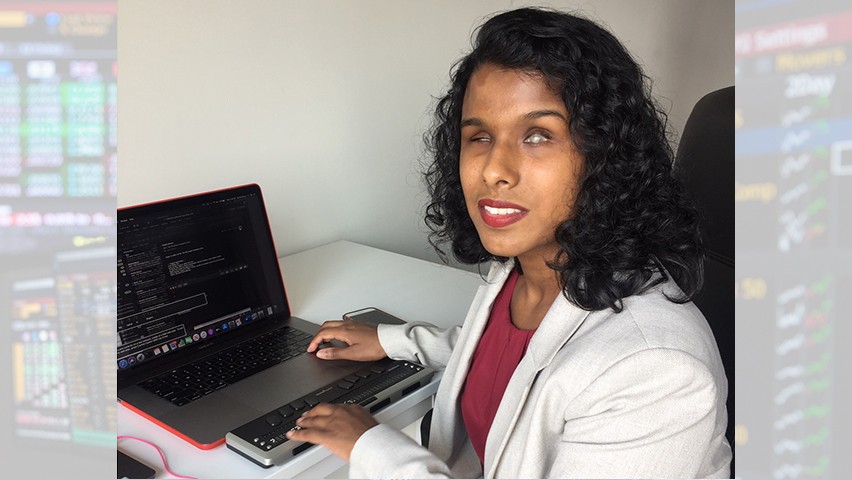 Shalini Menon sitting at her workstation, which includes a laptop and a refreshable braille reader.