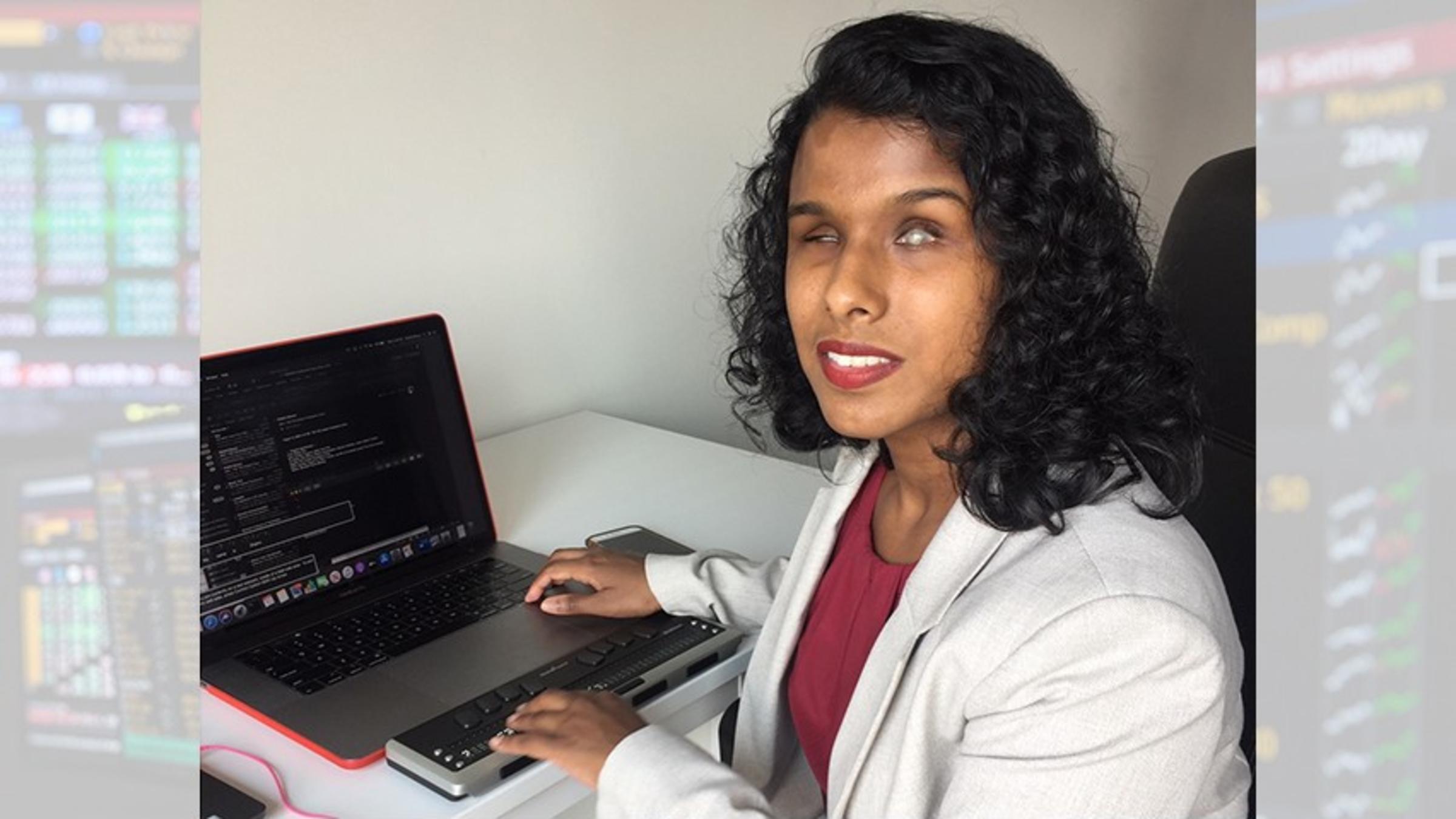 Shalini Menon sitting at her workstation, which includes a laptop and a refreshable braille reader.