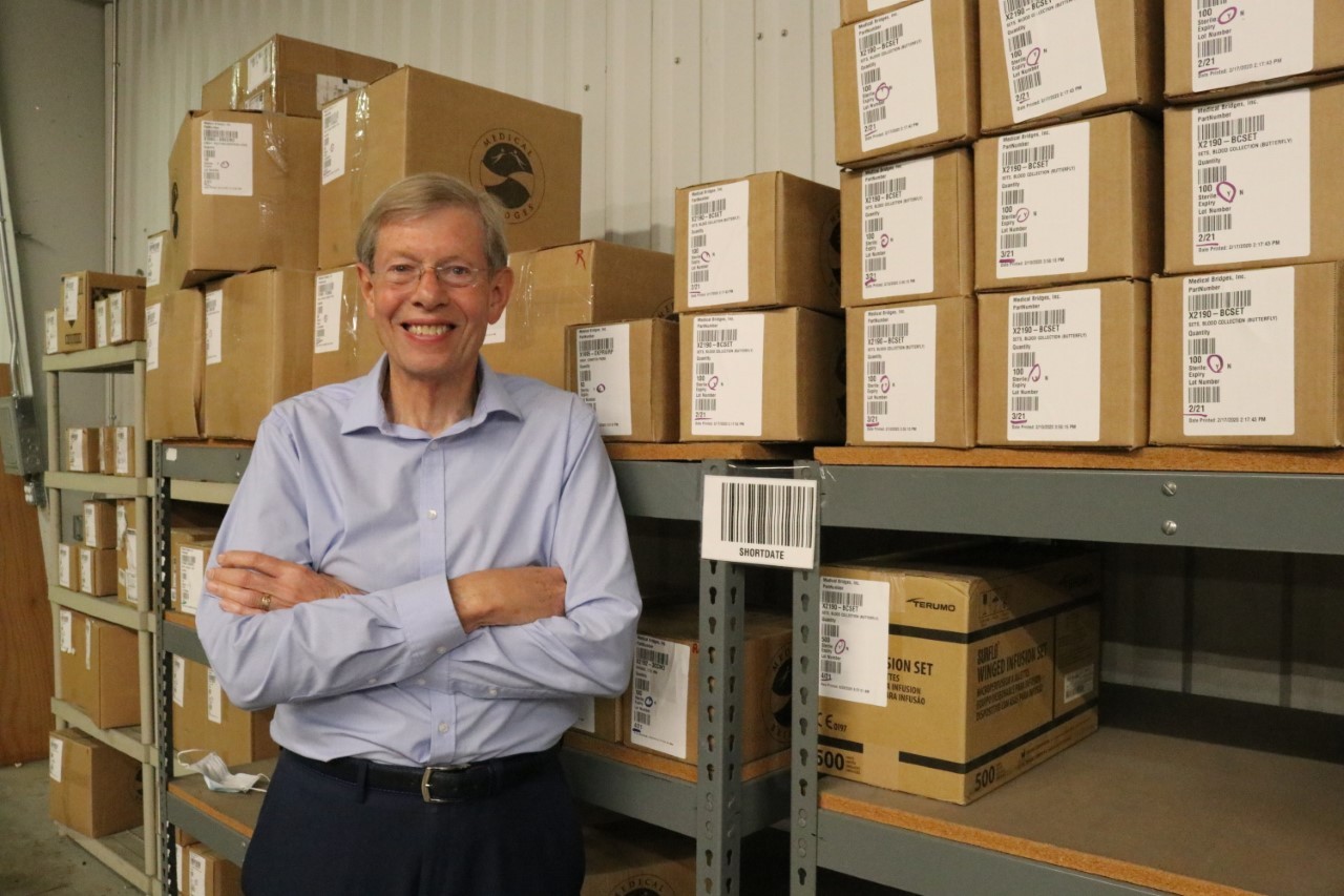Walter Ulrich '68 posing with stacks of boxes at the nonprofit's warehouse