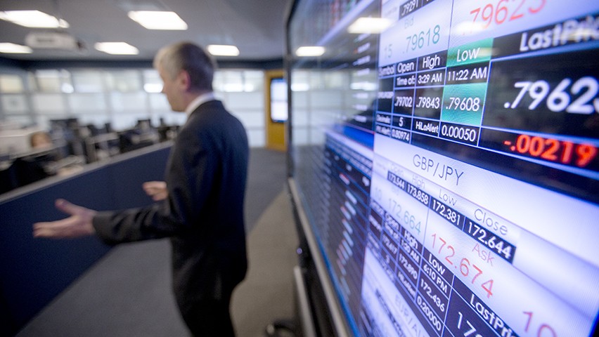 Screens in the Hanlon Lab showcase currency pricing data as a professor, dressed in a dark suit, gestures to the class.