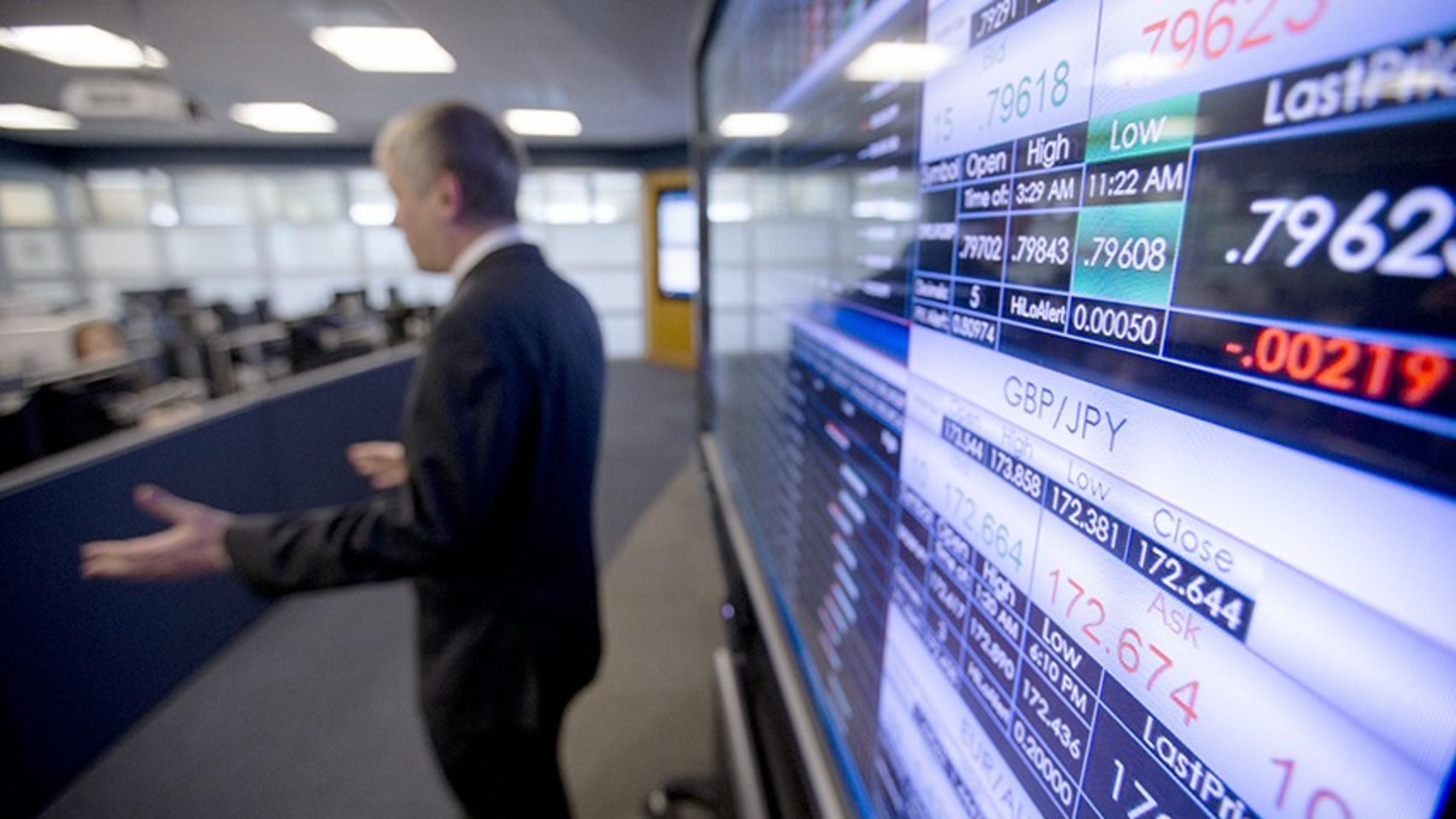 Screens in the Hanlon Lab showcase currency pricing data as a professor, dressed in a dark suit, gestures to the class.