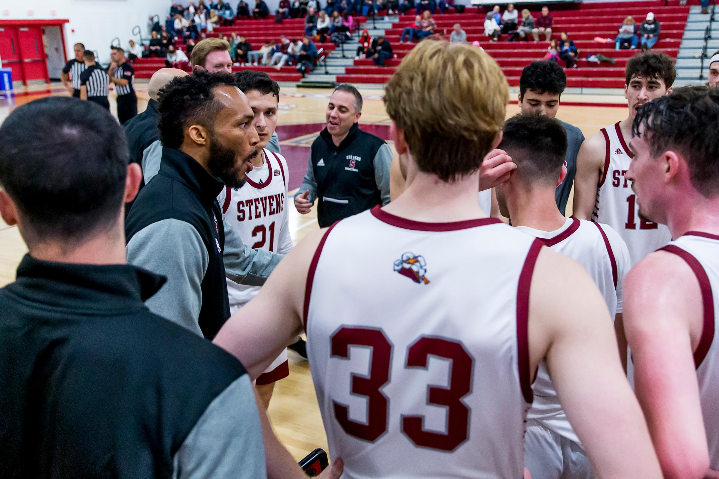 Michael Collins coaching the Stevens basketball team, as the players gather around him on the court