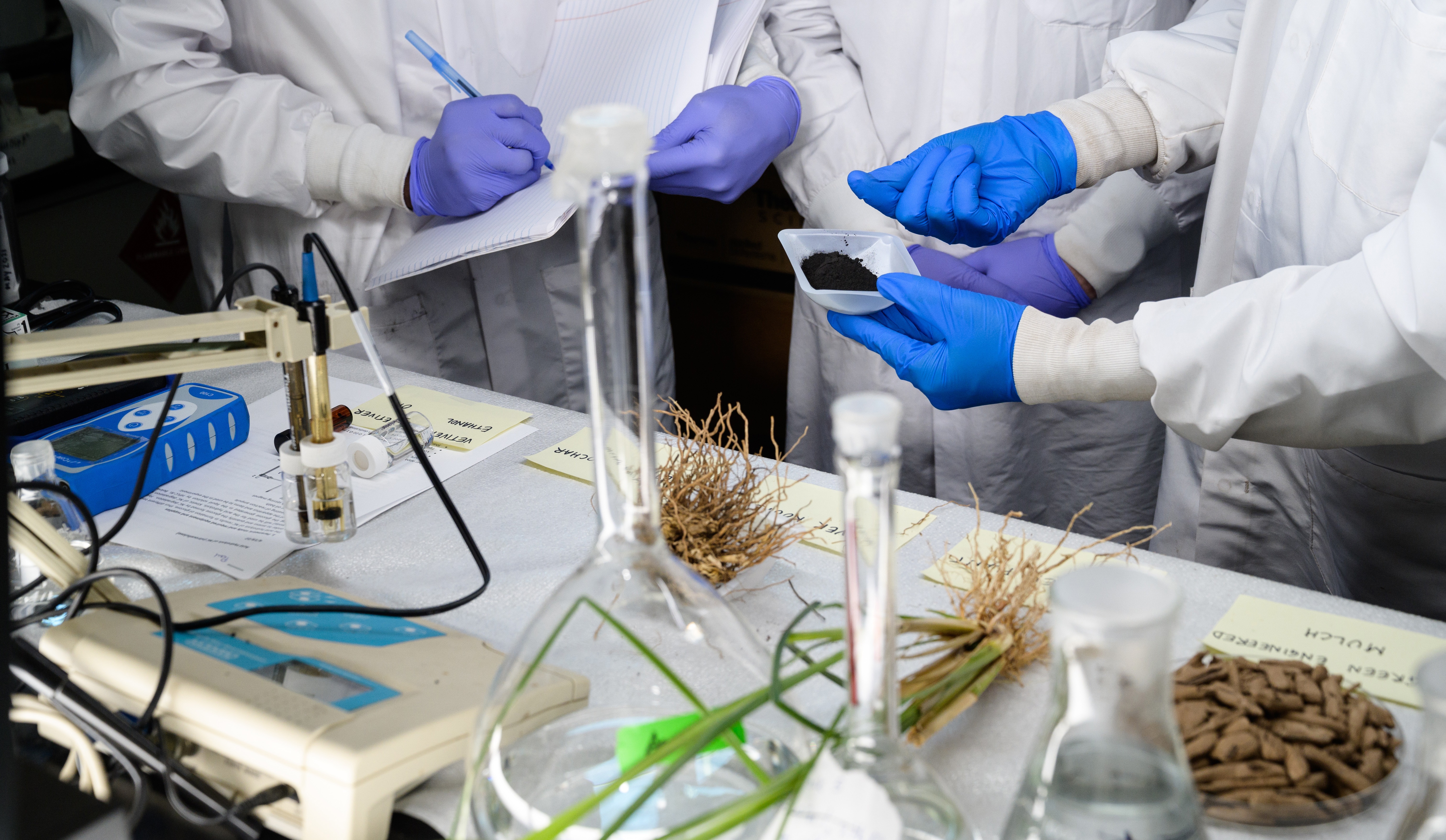 Three peoples hands and half bodies in lab gear with their experiments