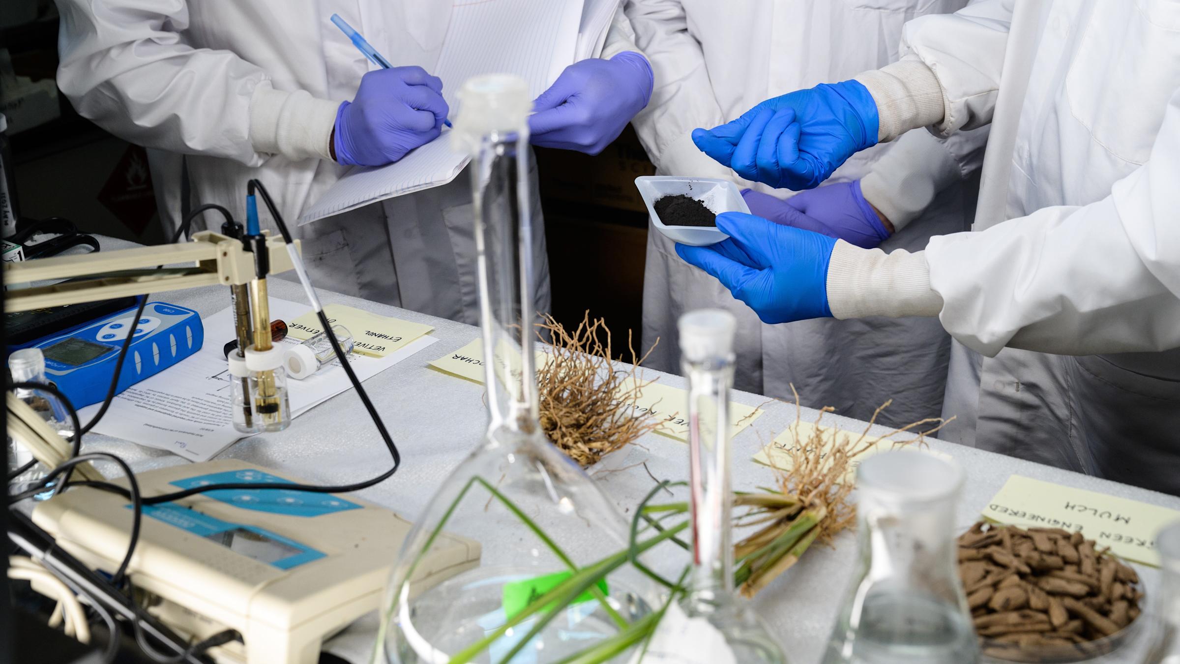 Three peoples hands and half bodies in lab gear with their experiments