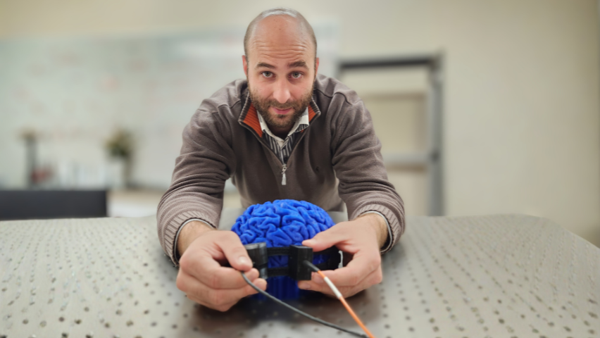 Simon Mahler holding the SCOS laser device on a 3D printed brain.