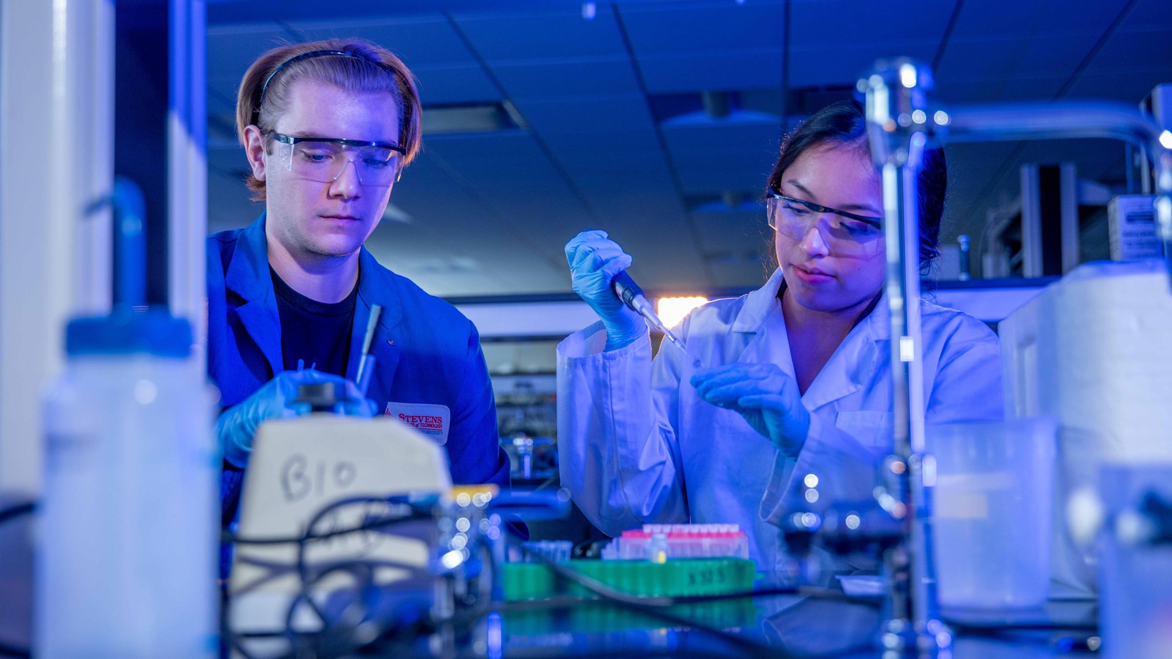 Two women in a lab with lab equipment performing an experiment.