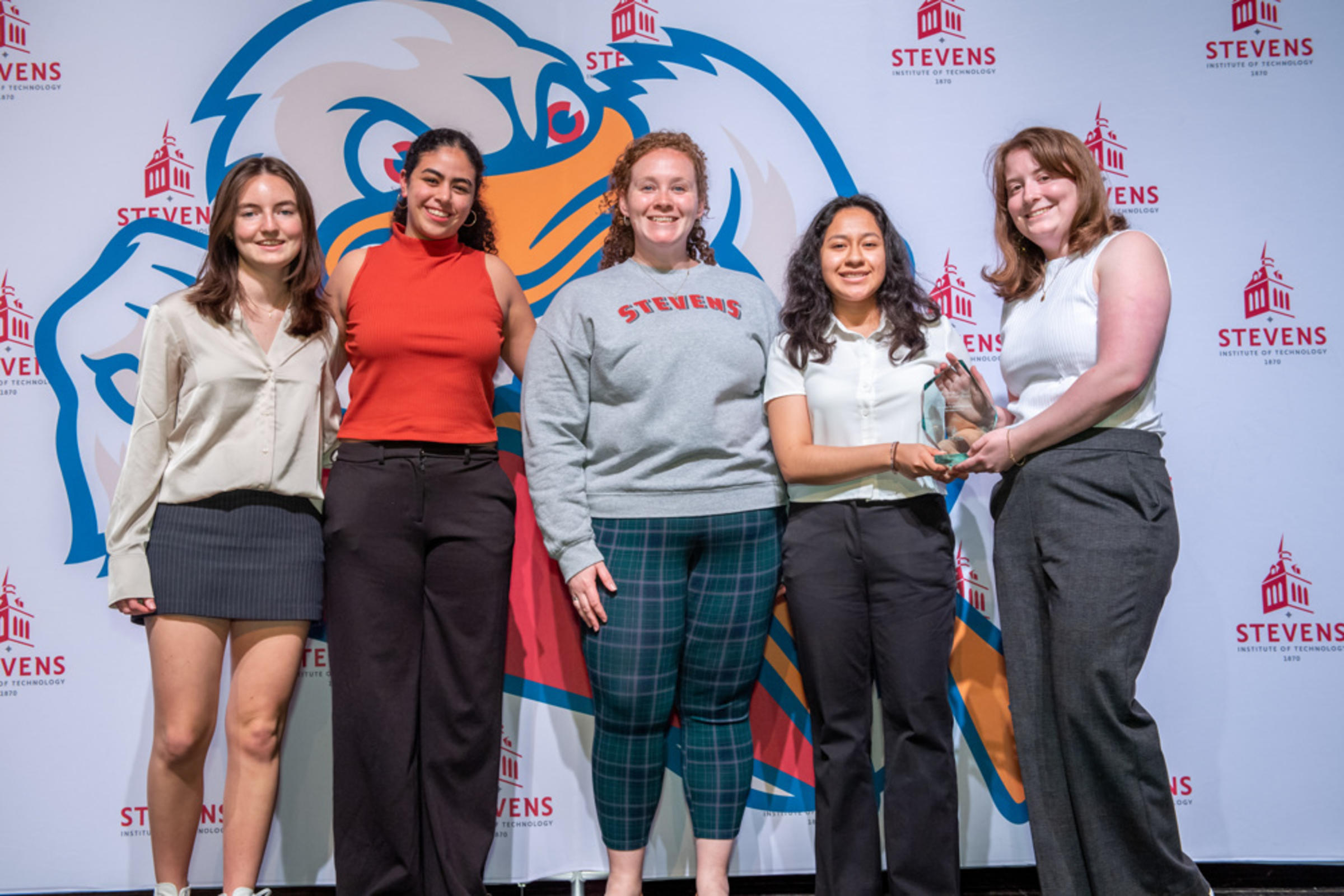 A photo of 5 young women standing together and holding an award
