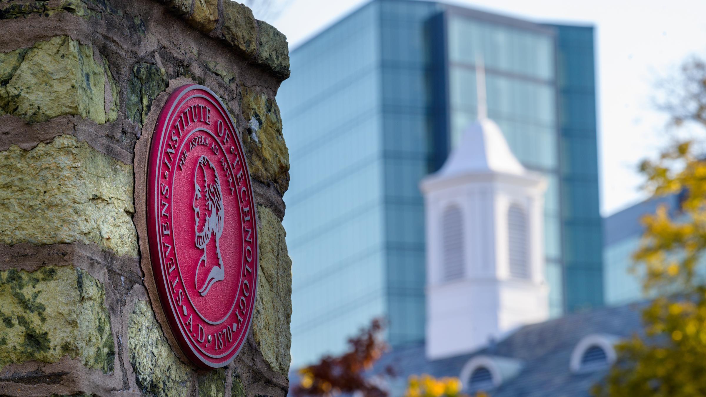 Stevens seal on gateway in foreground with buildings in background.