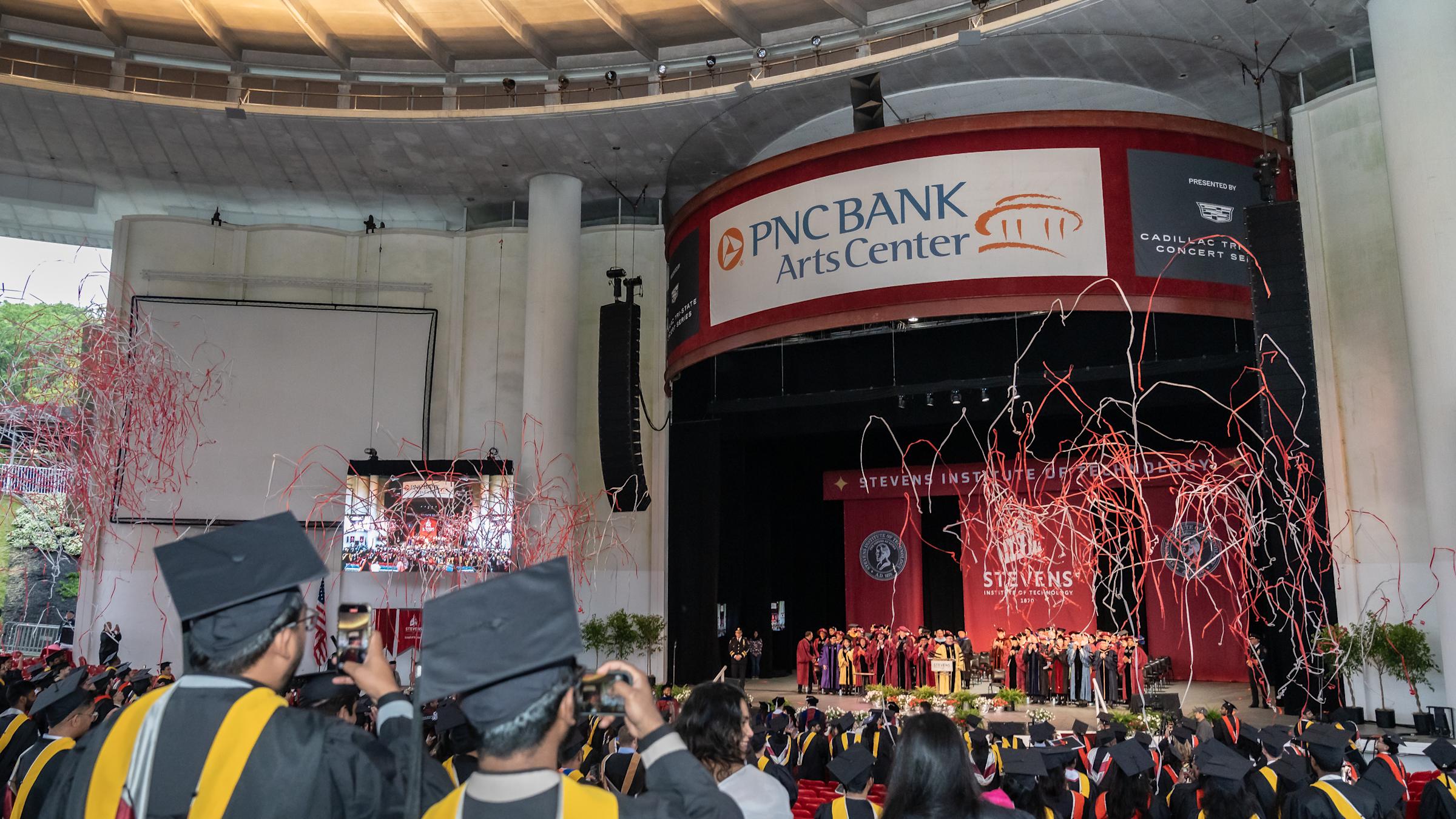 Students celebrate commencement as streamers shoot into the air.