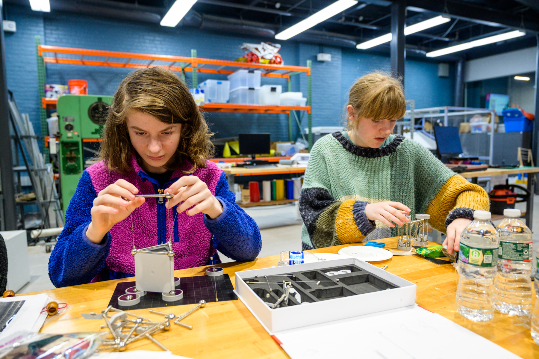 Two girls sit at a table assembling small towers from engineering supplies kits