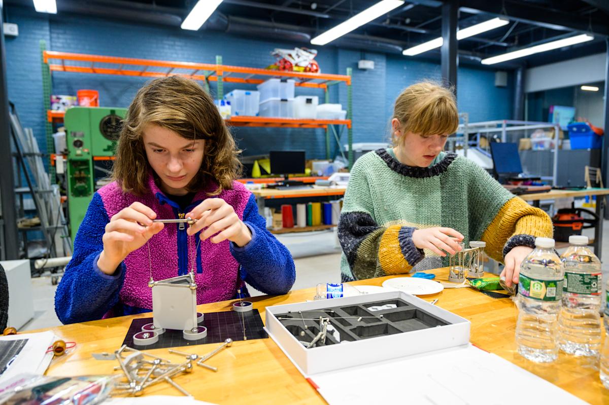 Two girls sit at a table assembling small towers from engineering supplies kits
