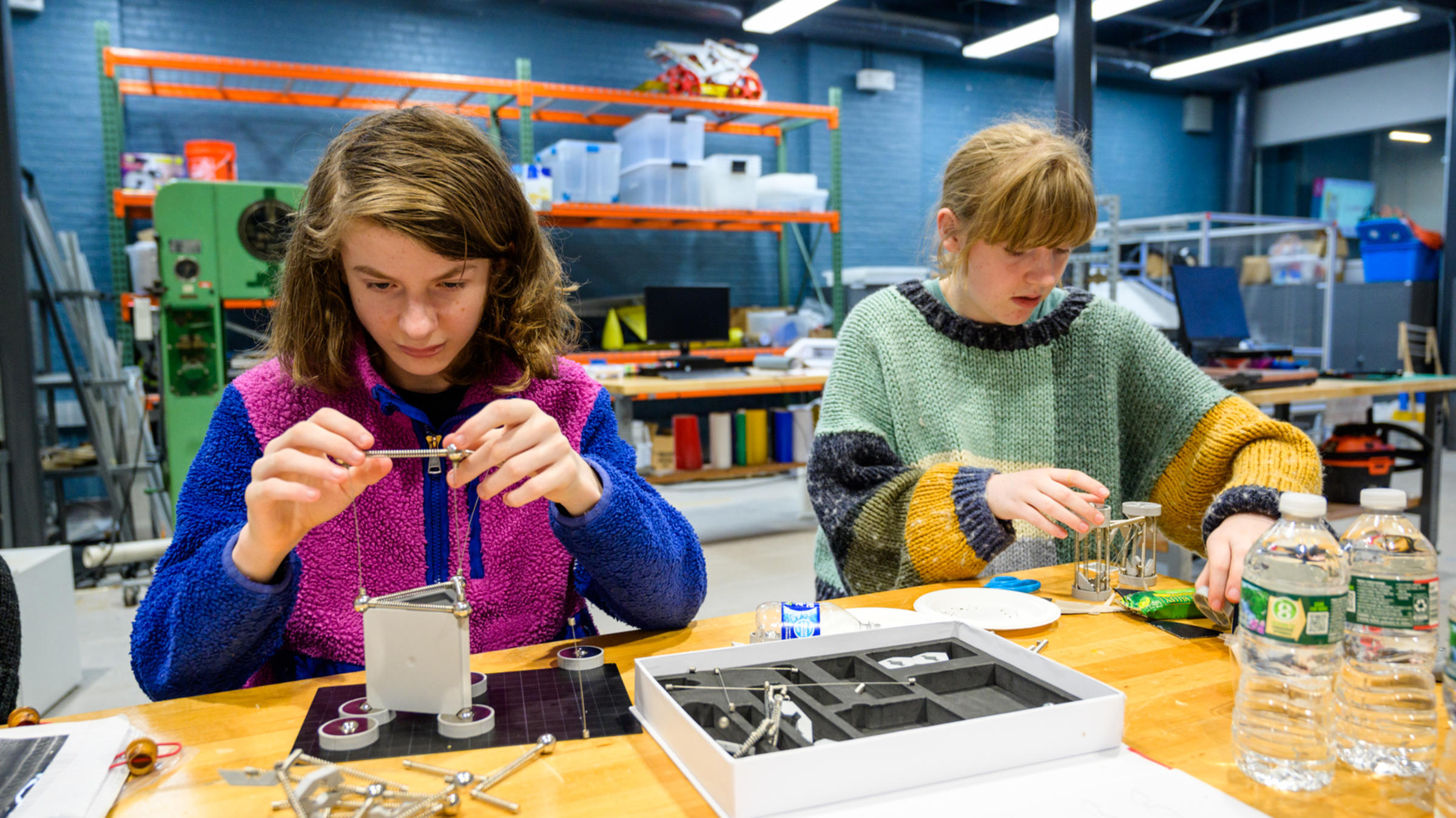 Two girls sit at a table assembling small towers from engineering supplies kits