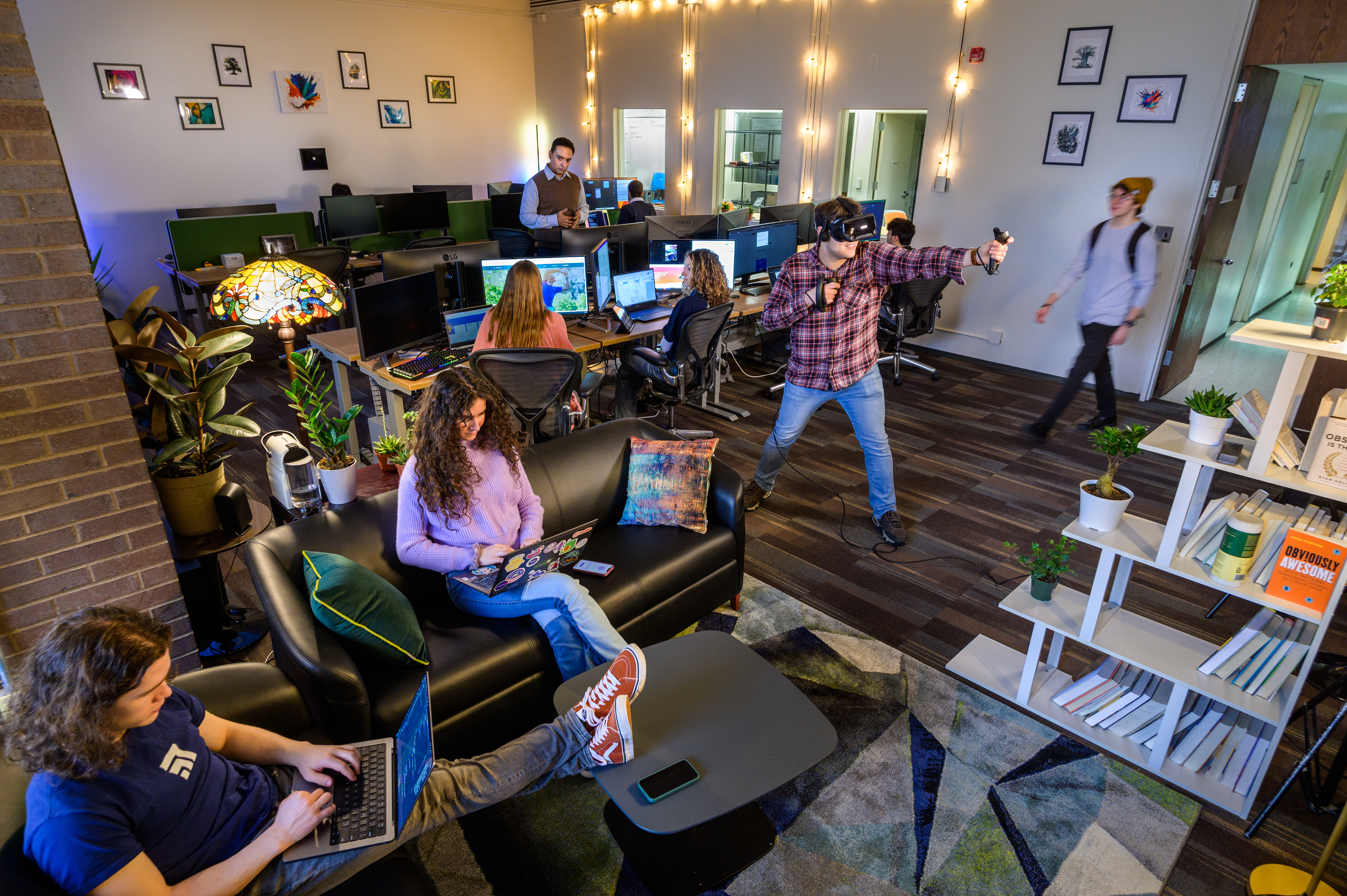 Students working in a lab, some on computers, one in a VR headset.