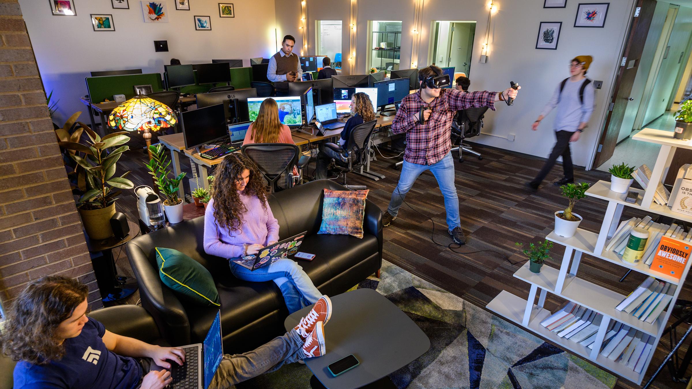 Students working in a lab, some on computers, one in a VR headset.
