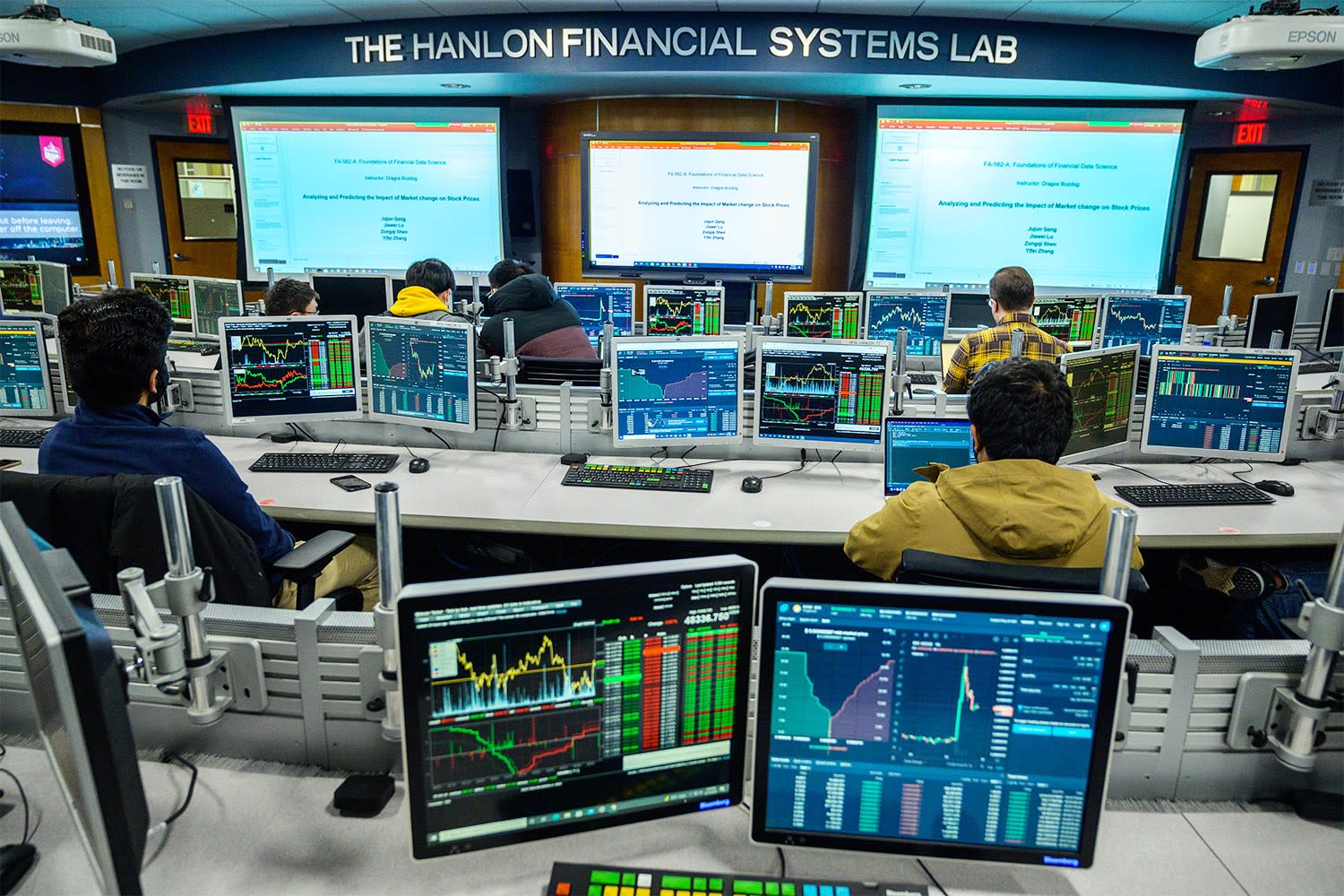 Students work at tiered trading desks in The Hanlon Financial Systems Lab, with multiple monitors displaying market data, charts, and financial analysis. 