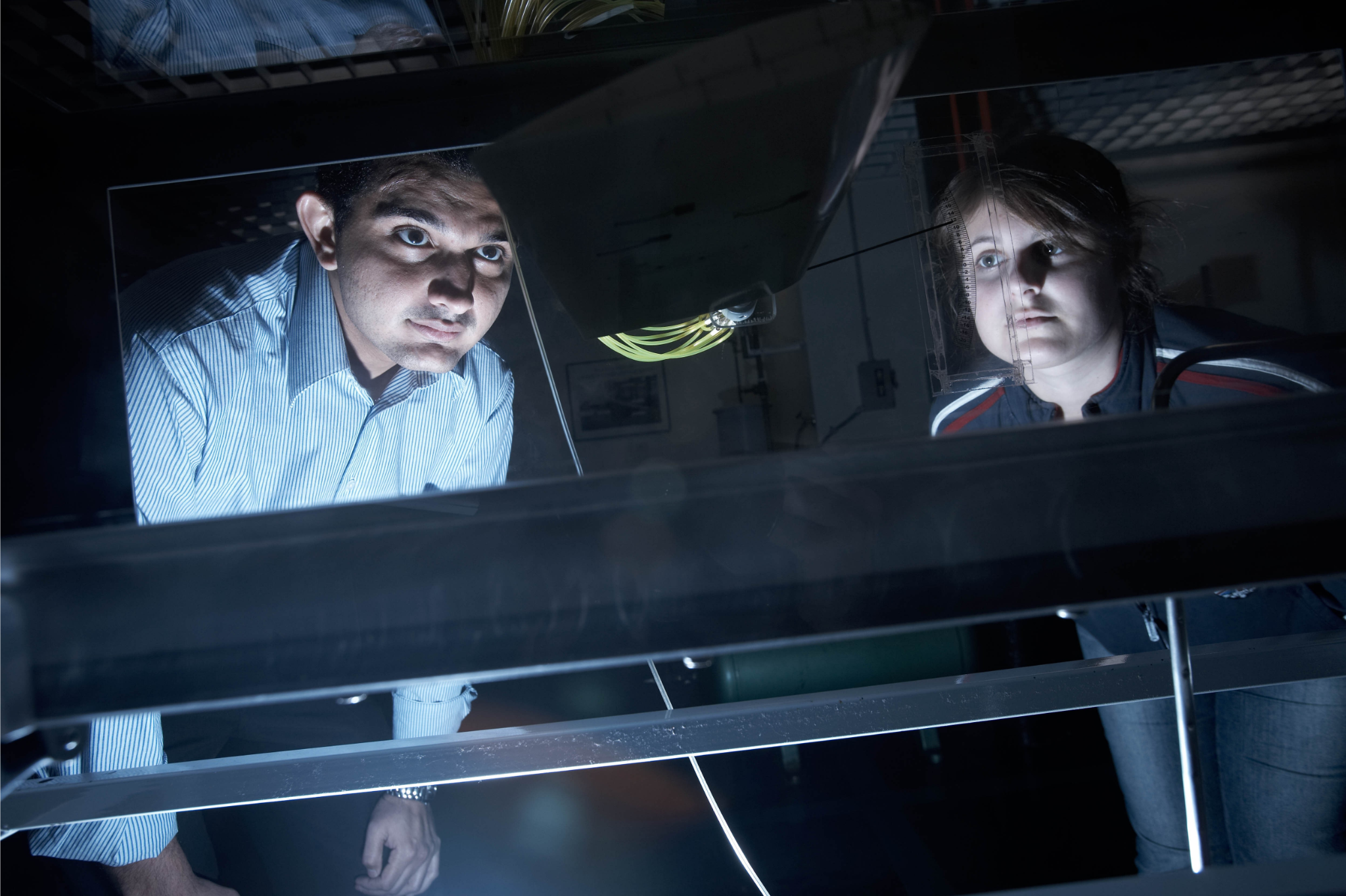 Two students observing an experiment in a dark Physics lab.