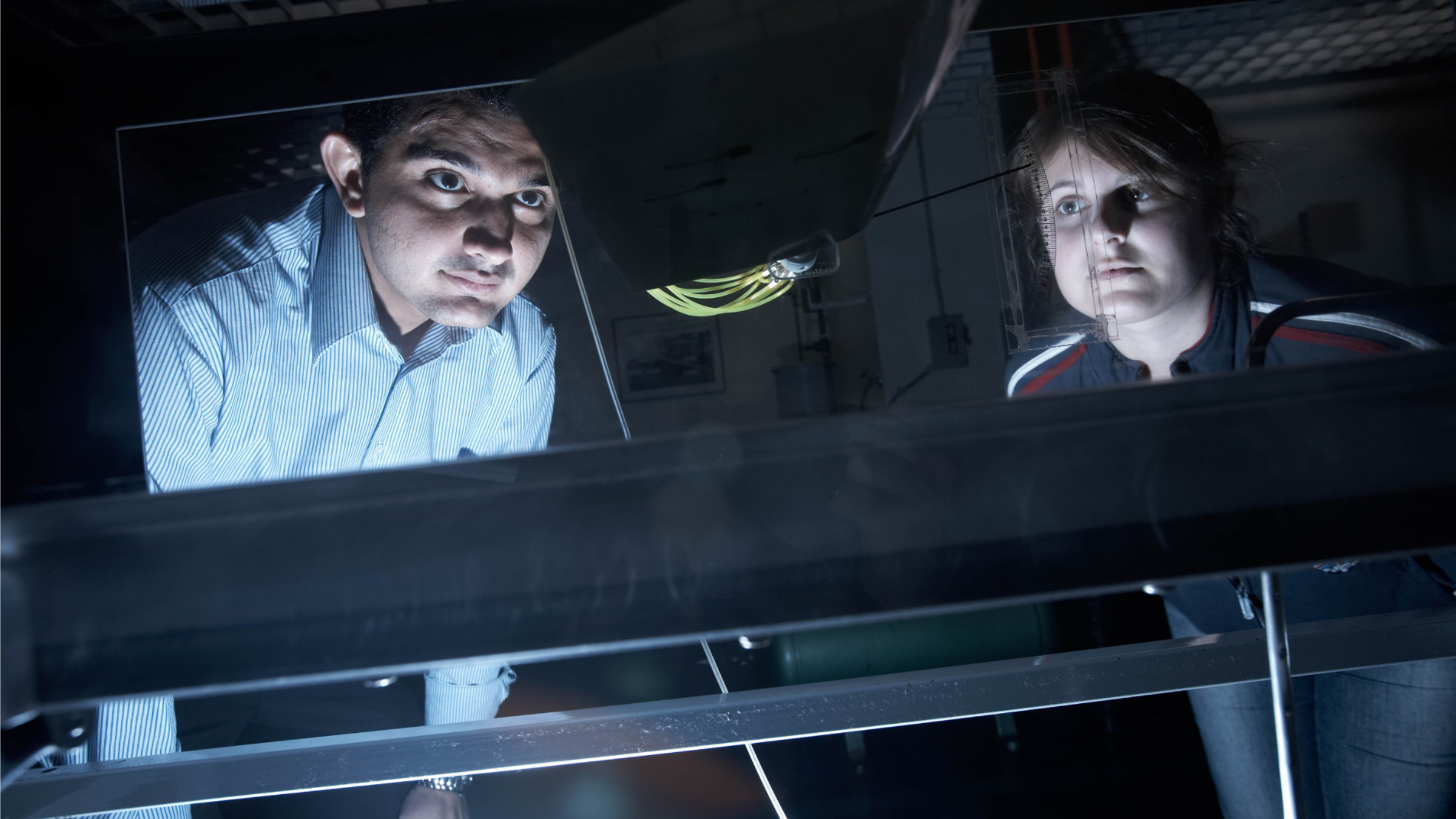 Two students observing an experiment in a dark Physics lab.