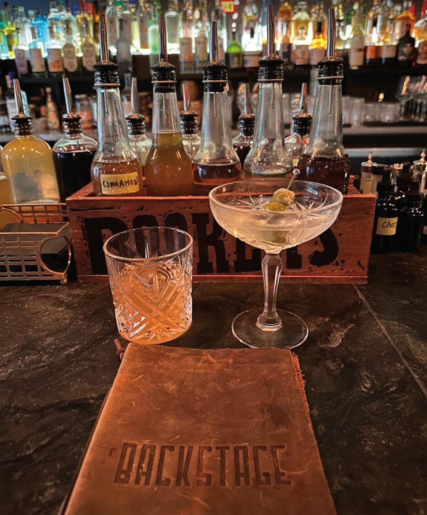 two cocktails on a bar, with bottles hanging in the background and a menu that says Back Stage in the foreground.