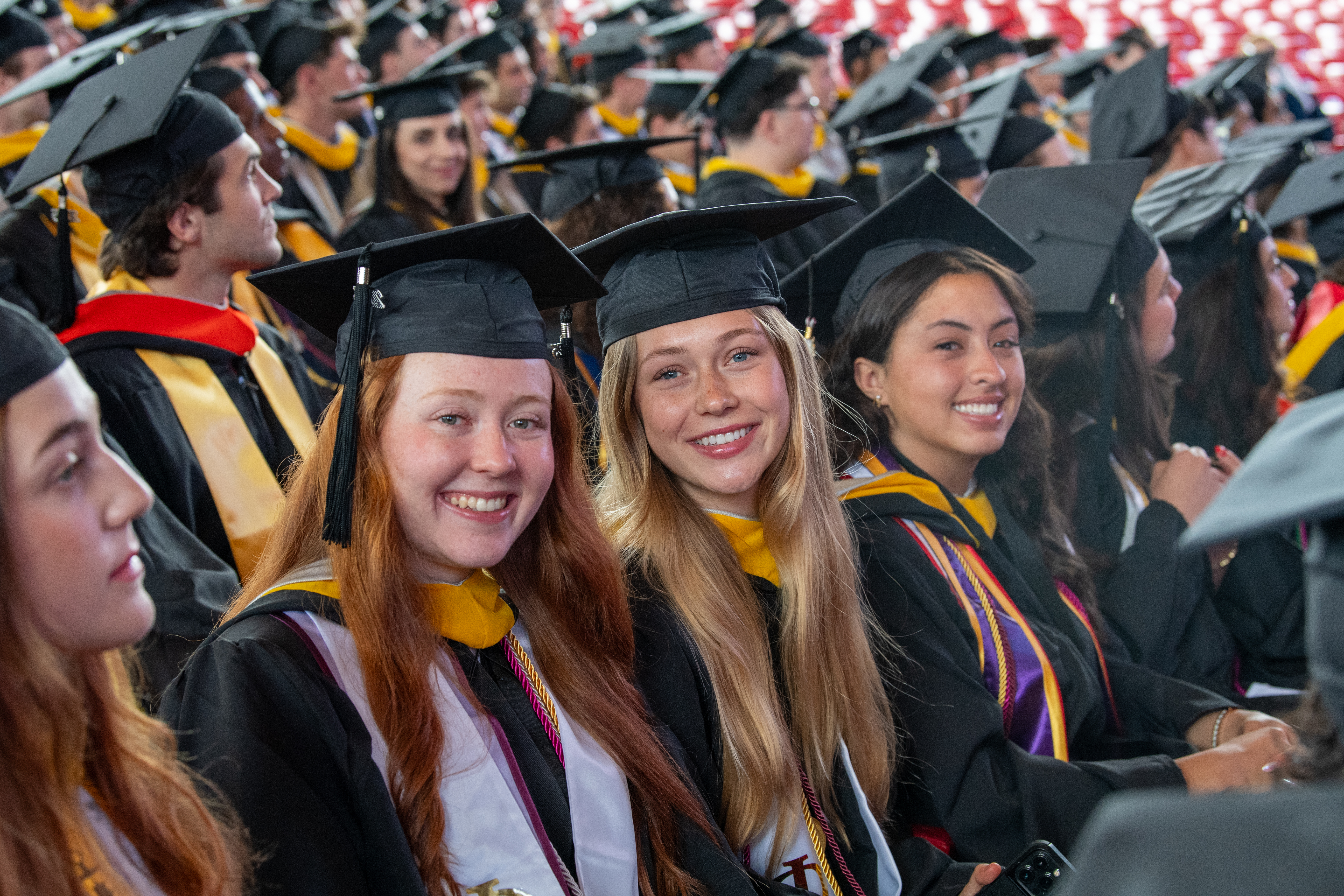 The women undergraduate students dressed in commencement regalia smile.