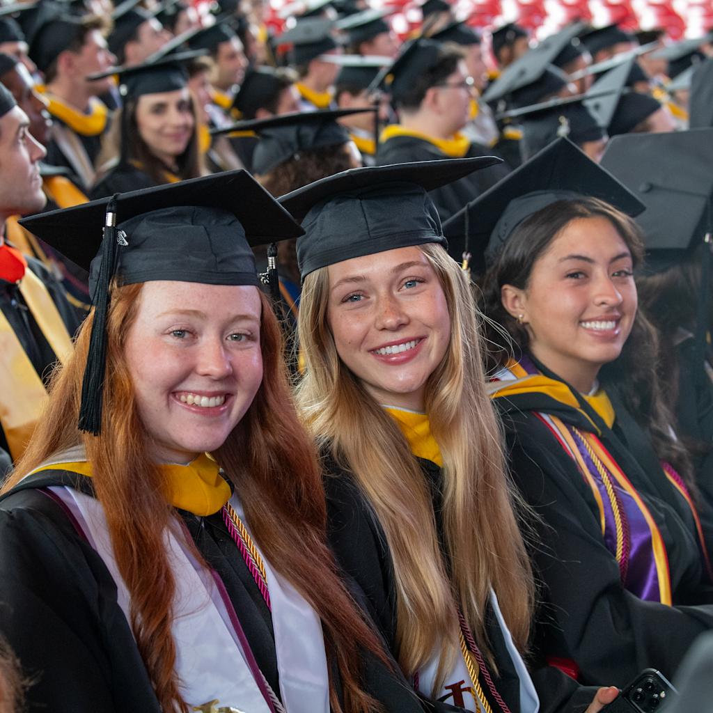 The women undergraduate students dressed in commencement regalia smile.