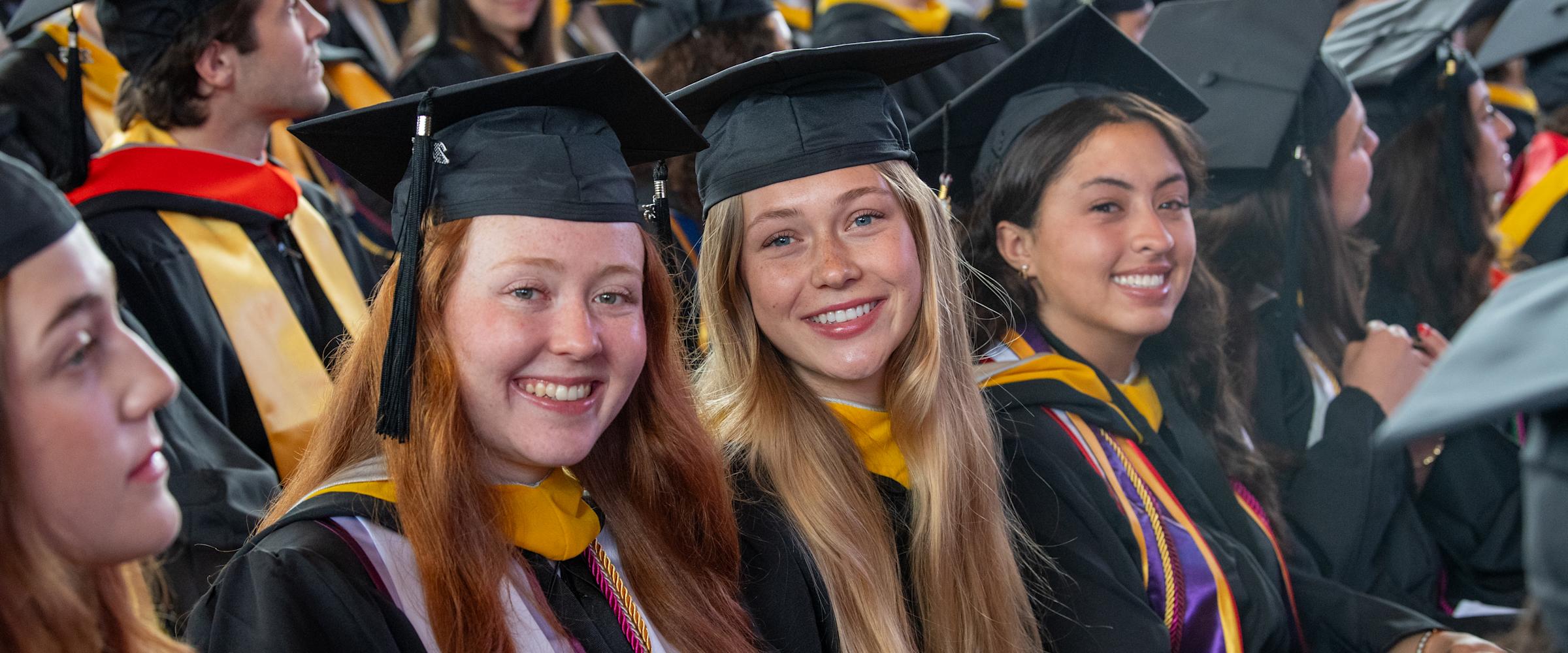 The women undergraduate students dressed in commencement regalia smile.