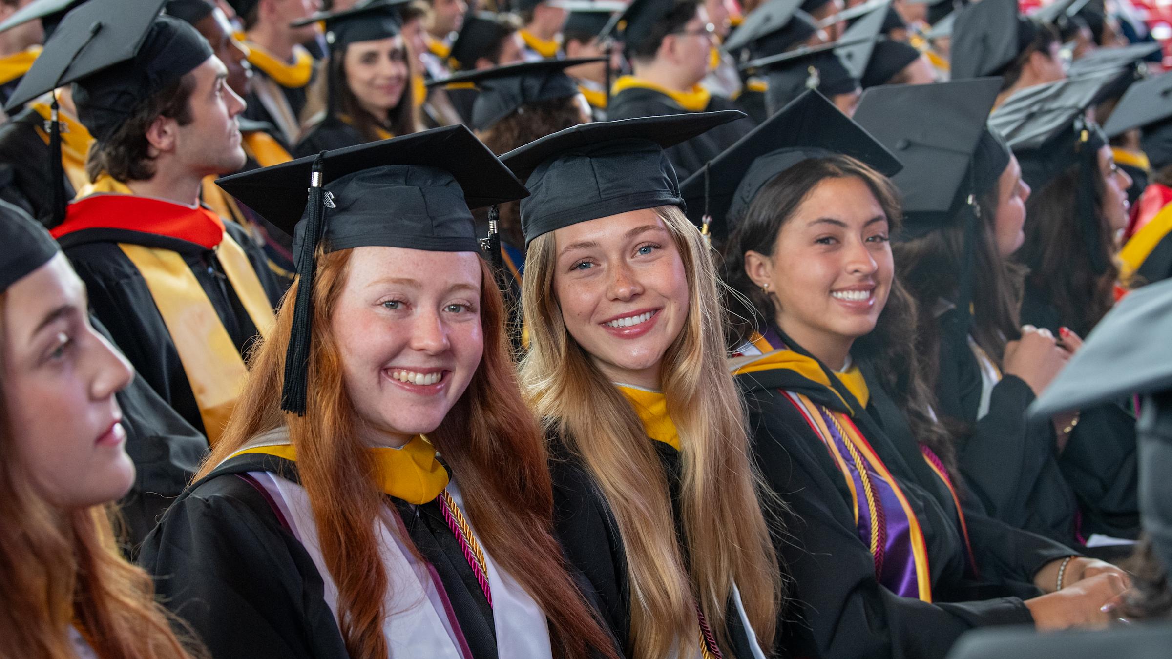 The women undergraduate students dressed in commencement regalia smile.