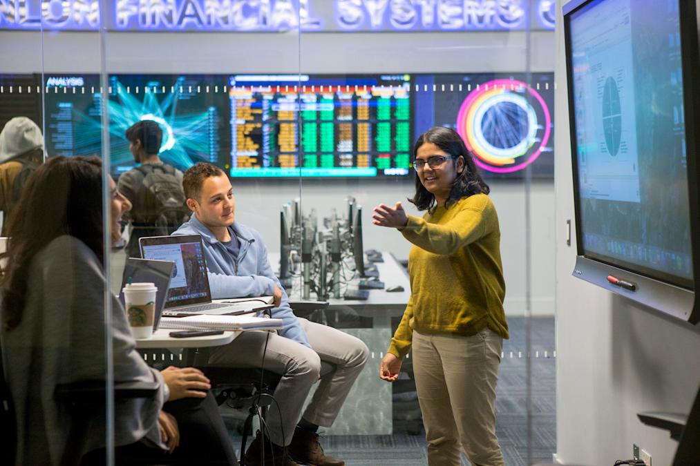 Student gestures to other students in front of monitors displaying data