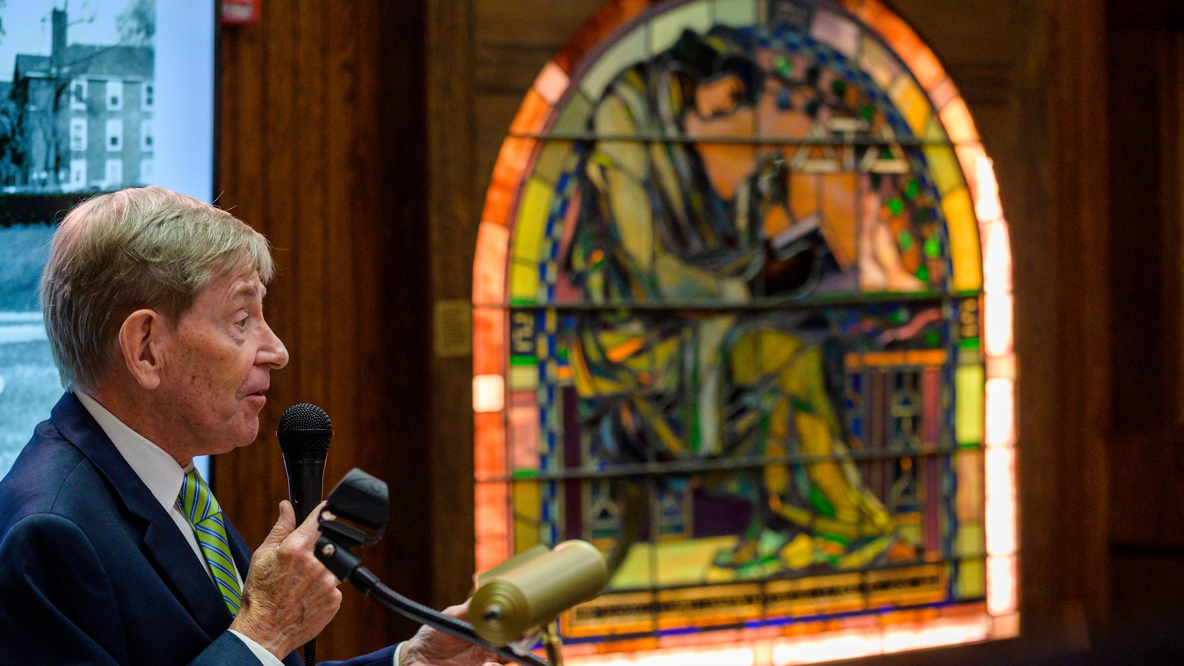 John Dalton stands at the Delta Tau Delta Wall of Achievement in the library