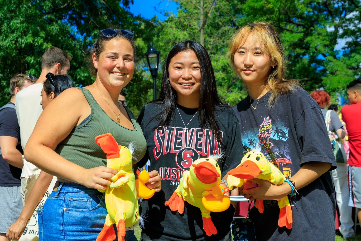 Three students smile and hold stuffed animal ducks