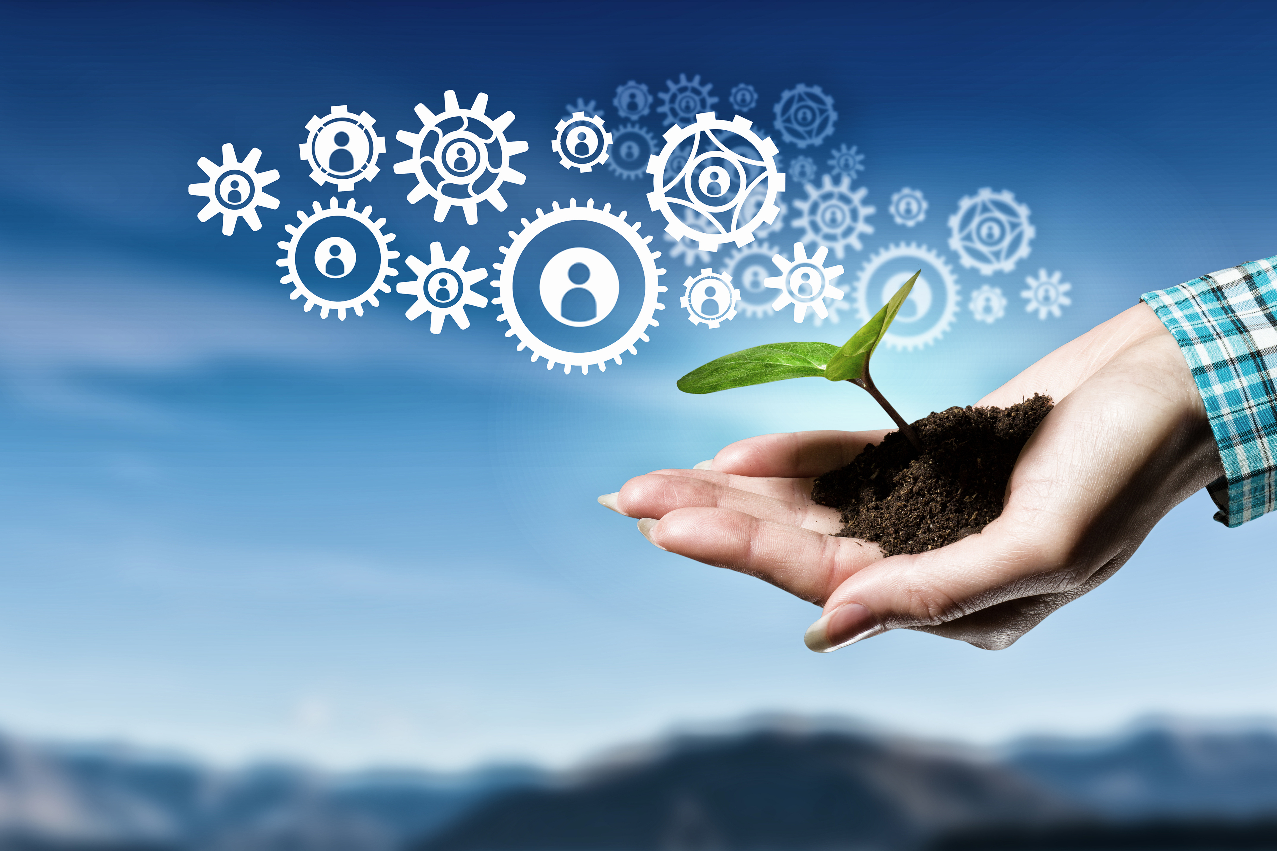 A hand holds a plant growing from soil, and coming from it are icons of gears. In the background is the sky.