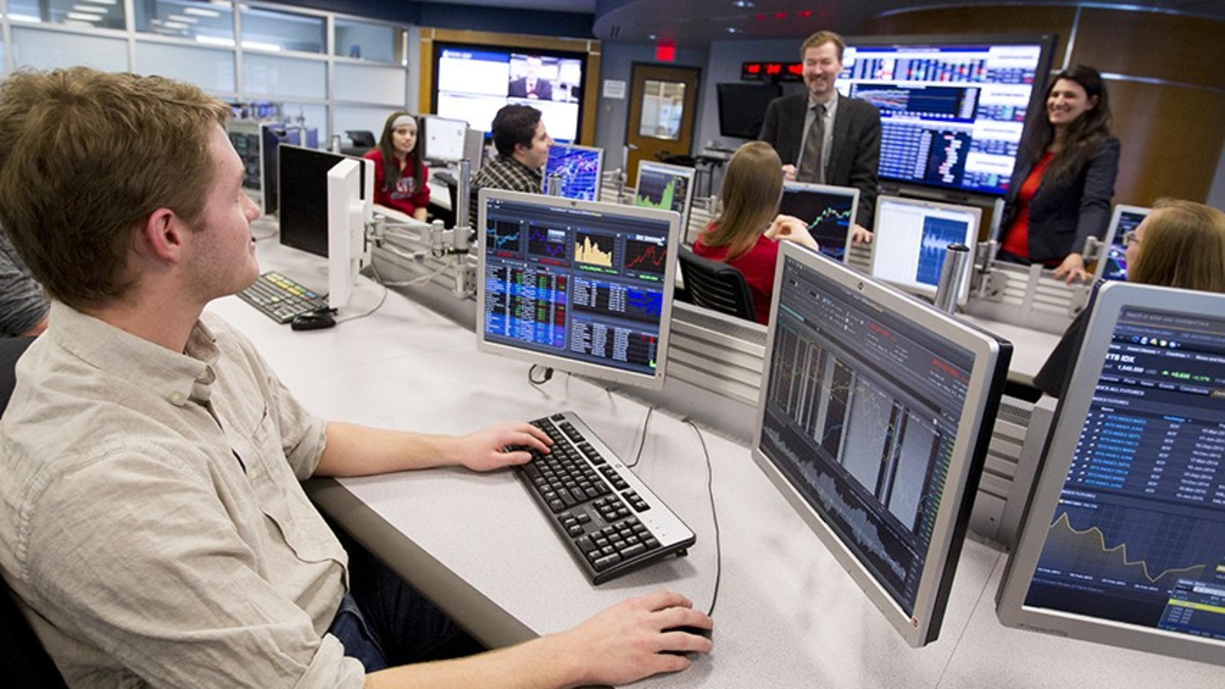 A finance class taking place in the Hanlon Financial Systems Center. A male student is asking a question of a female faculty member.