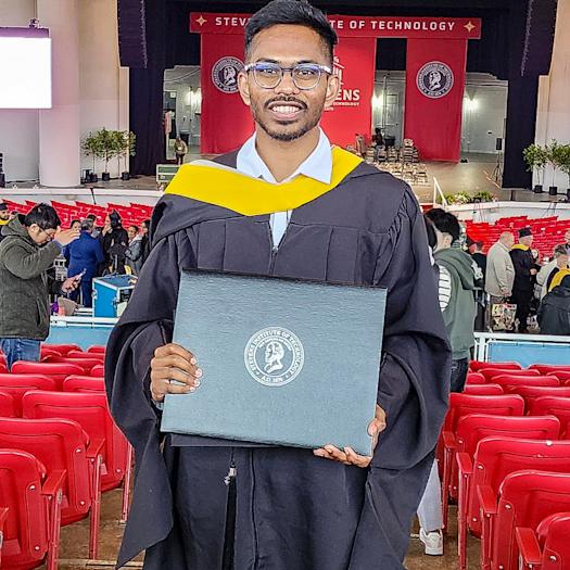 Aaryan Yekkisetty holds up his diploma wearing his black gown at his Stevens Institute of Technology graduation.