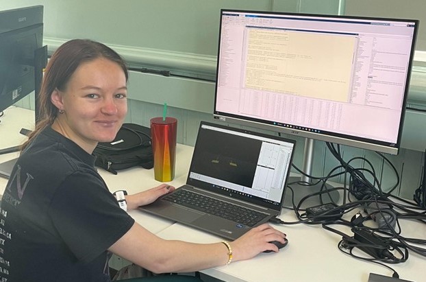 Photo of Samantha Gajda smiling at the camera while working on a computer