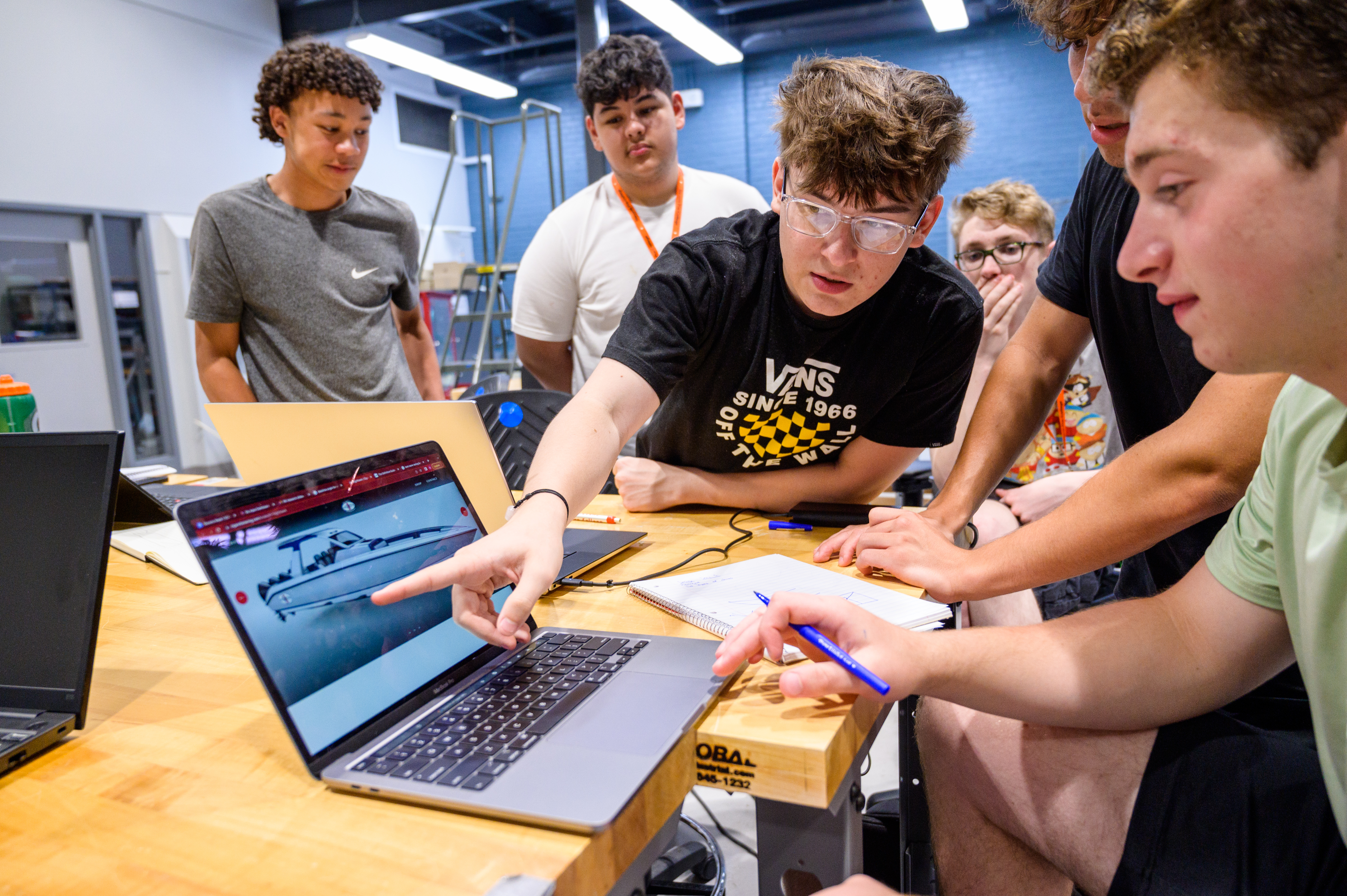 Pre-College students gathering around and looking at a students laptop which shows a boat.