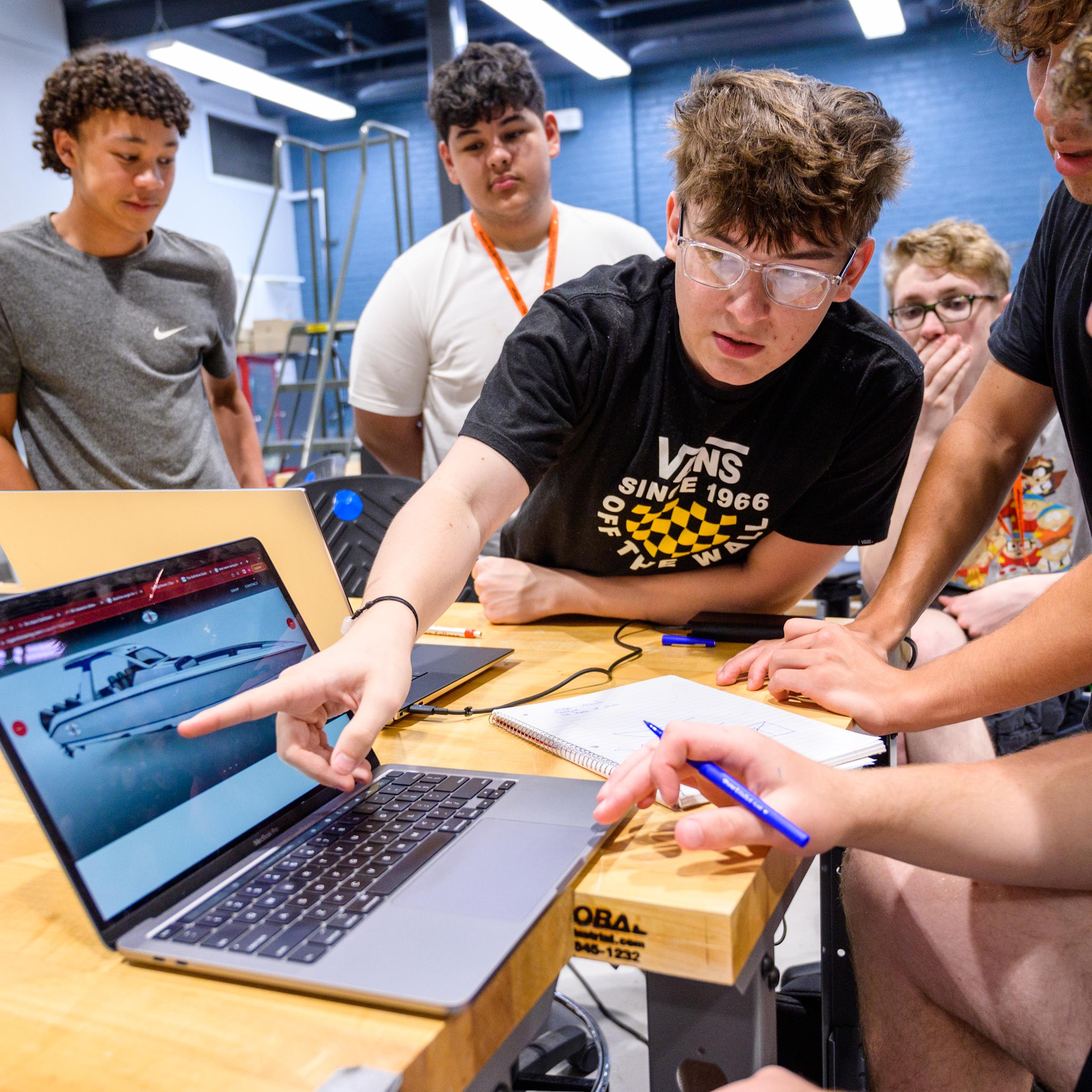 Pre-College students gathering around and looking at a students laptop which shows a boat.