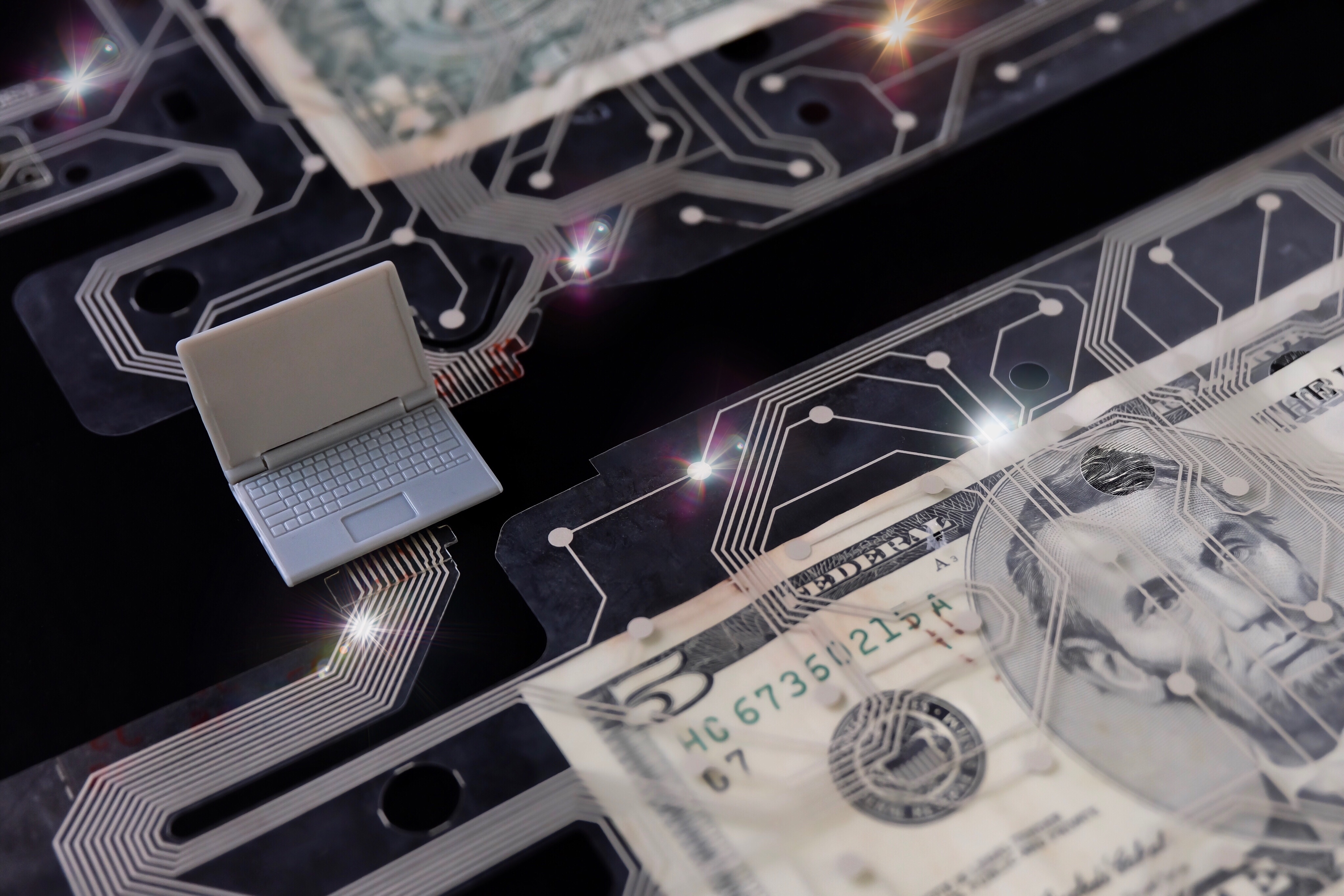 Representation of digital money with a plastic laptop, $5 bill and circuit board.