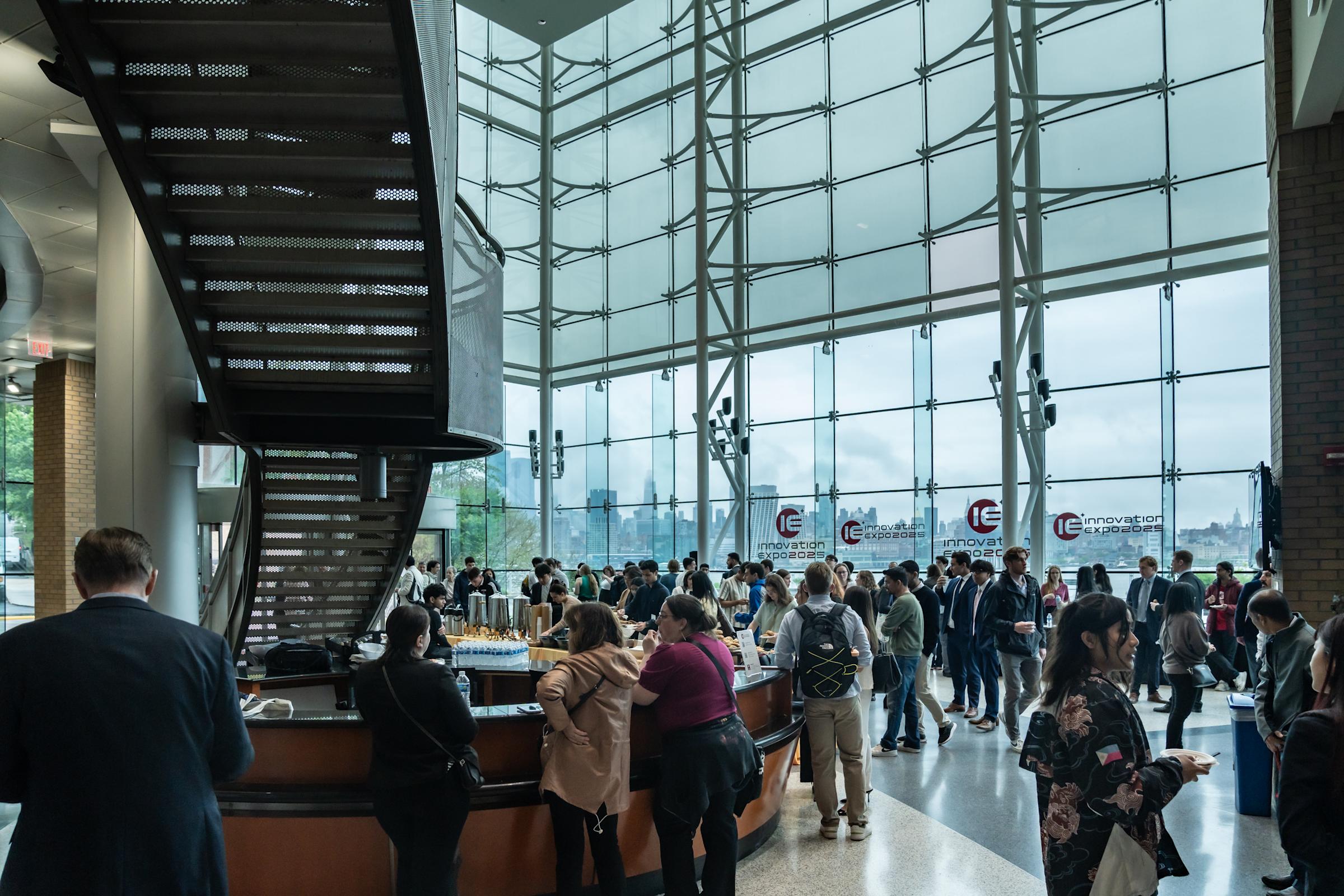 A wide shot of the Babbio Center atrium with a large group of people exploring the senior design projects.