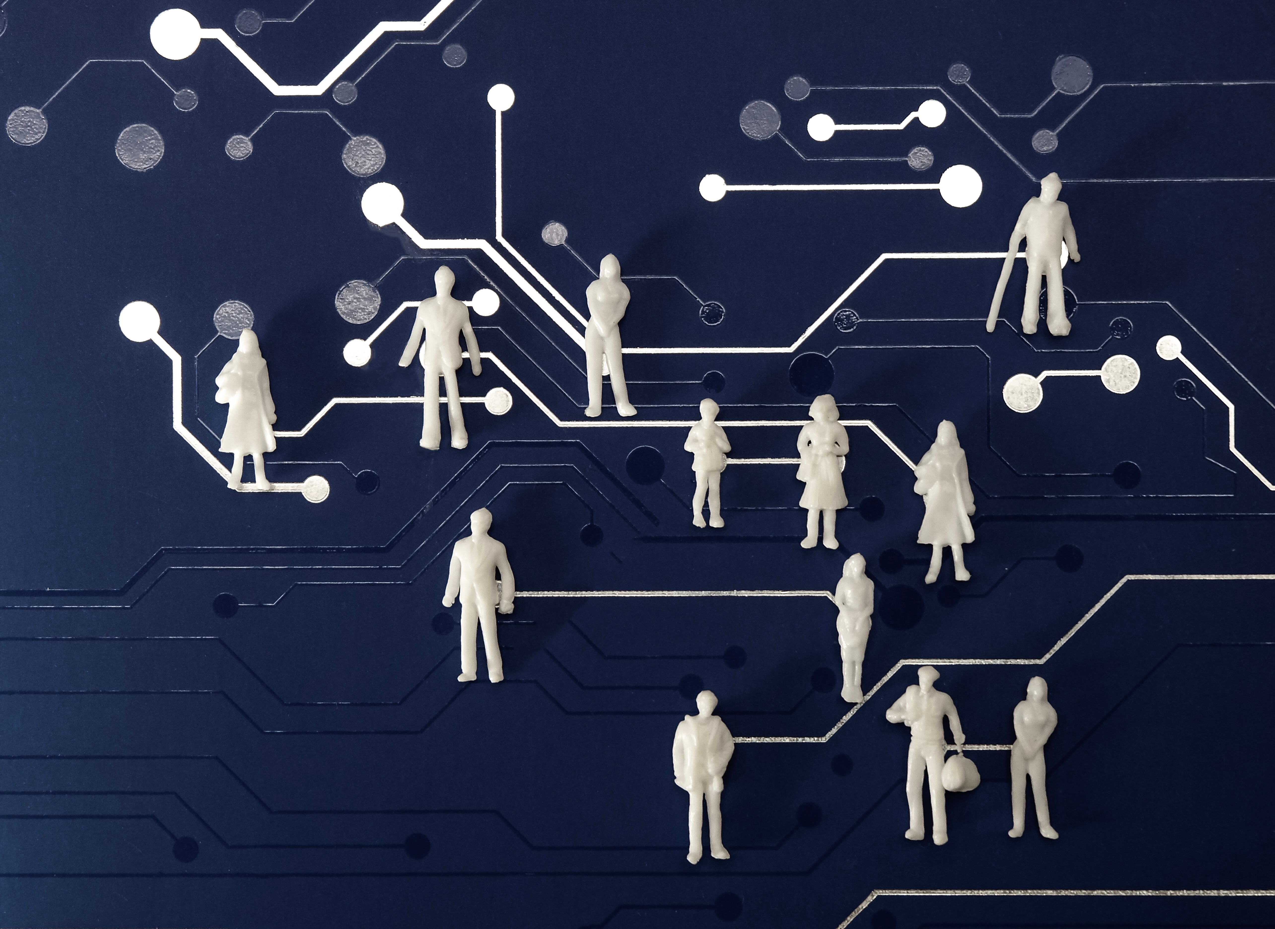 A collection of small, white, unidentifiable figures stand atop a blue surface patterned with white lines and circles that resemble a circuit board. 