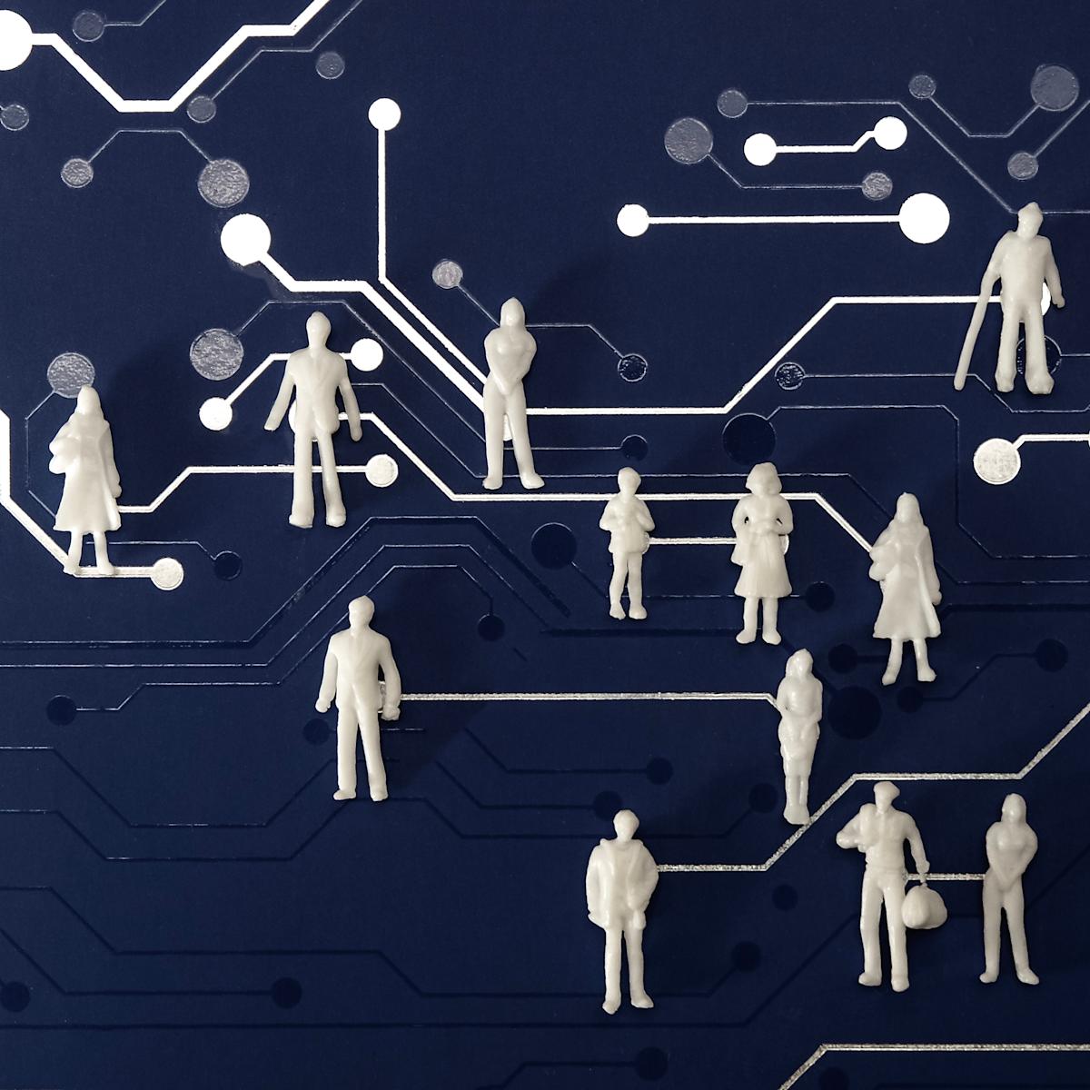 A collection of small, white, unidentifiable figures stand atop a blue surface patterned with white lines and circles that resemble a circuit board.