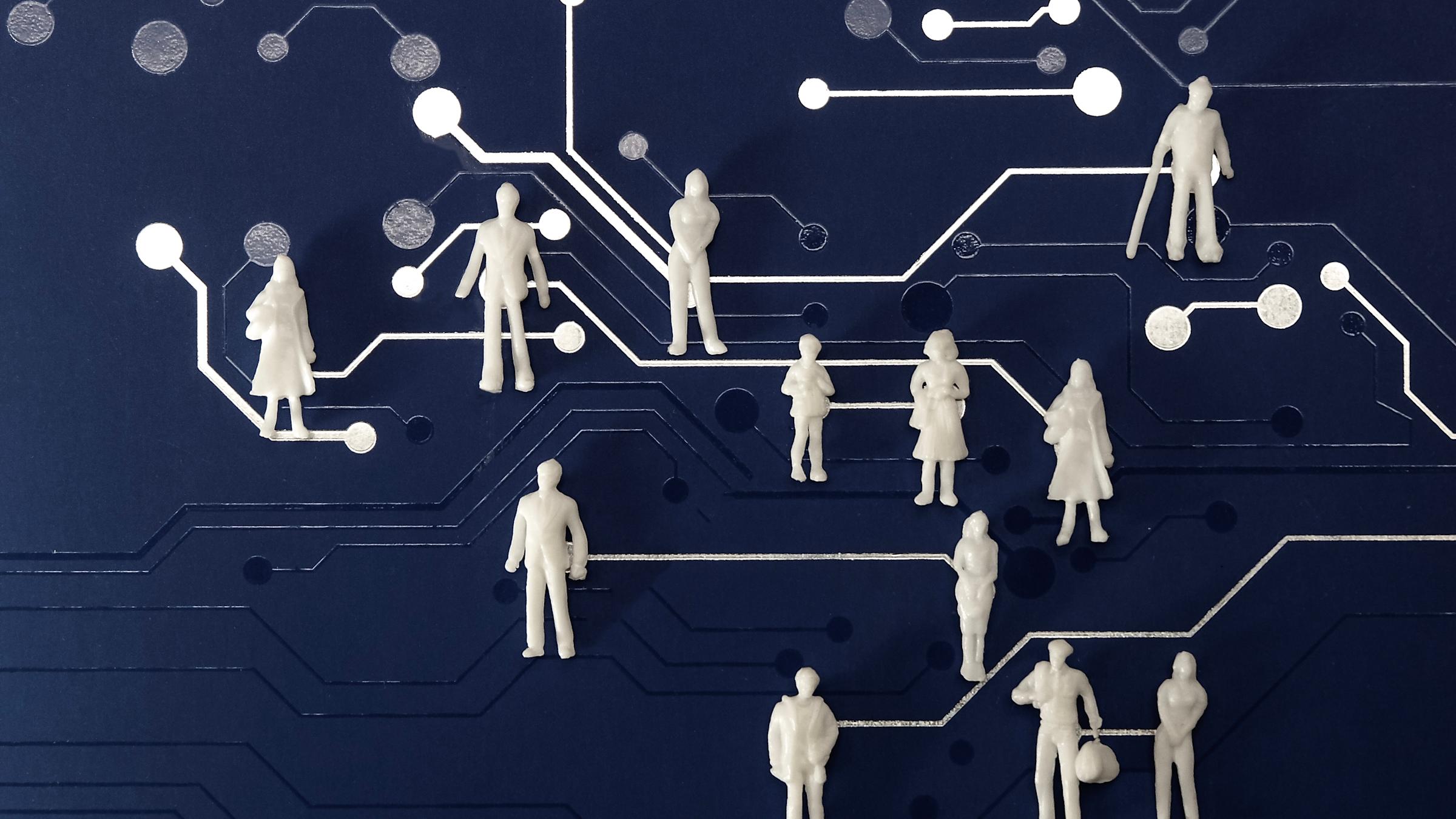 A collection of small, white, unidentifiable figures stand atop a blue surface patterned with white lines and circles that resemble a circuit board.