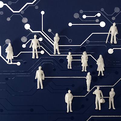 A collection of small, white, unidentifiable figures stand atop a blue surface patterned with white lines and circles that resemble a circuit board.