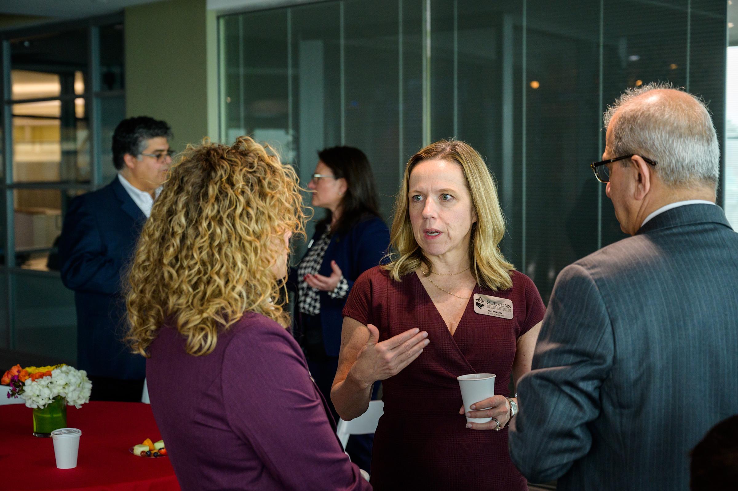 Professor Ann Murphy faces the camera while having a discussion with a woman in a purple blazer and Stevens president Nariman Farvardin.