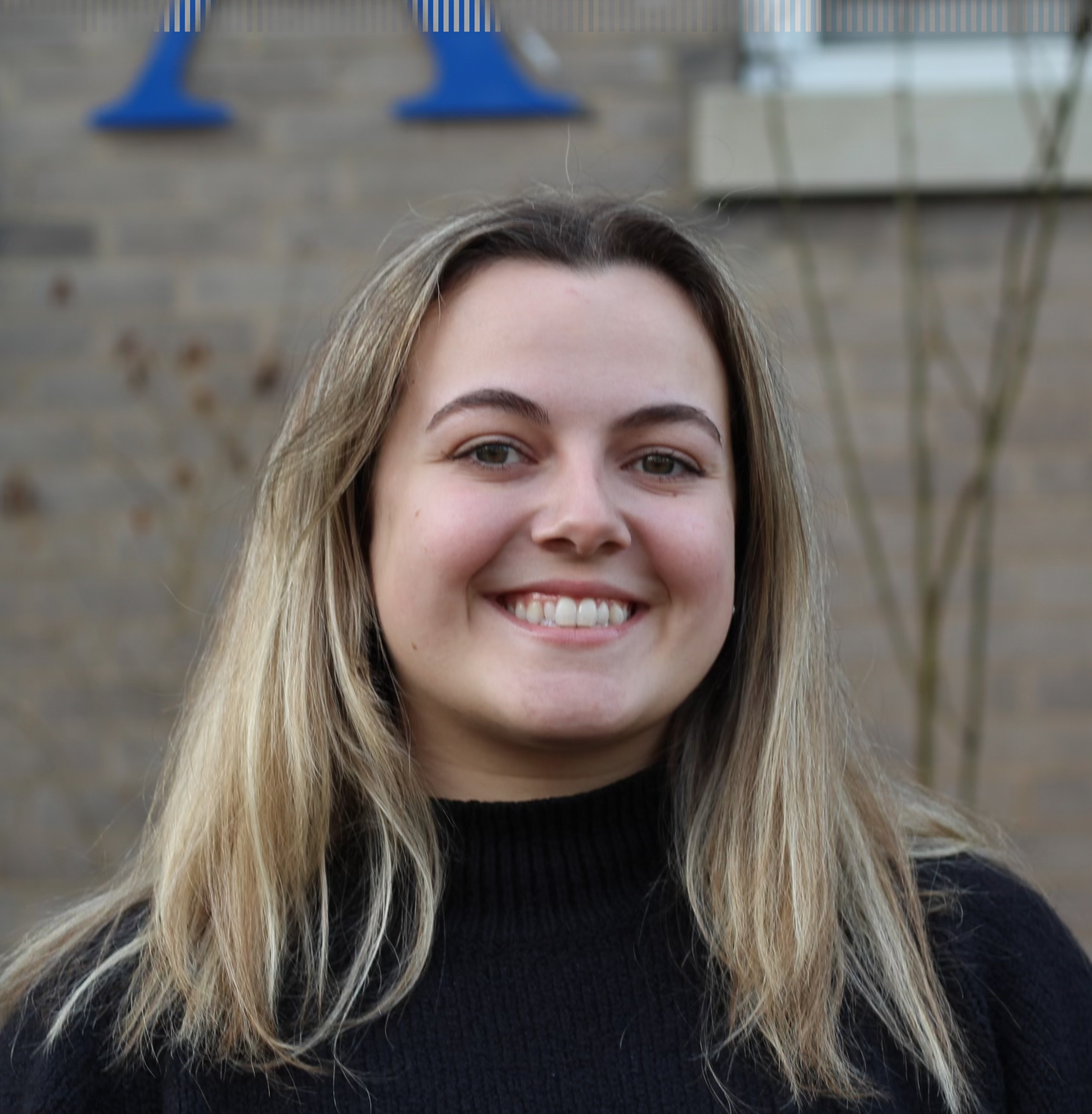 A headshot of Laura Masciola taken outside in front of a building and some plants