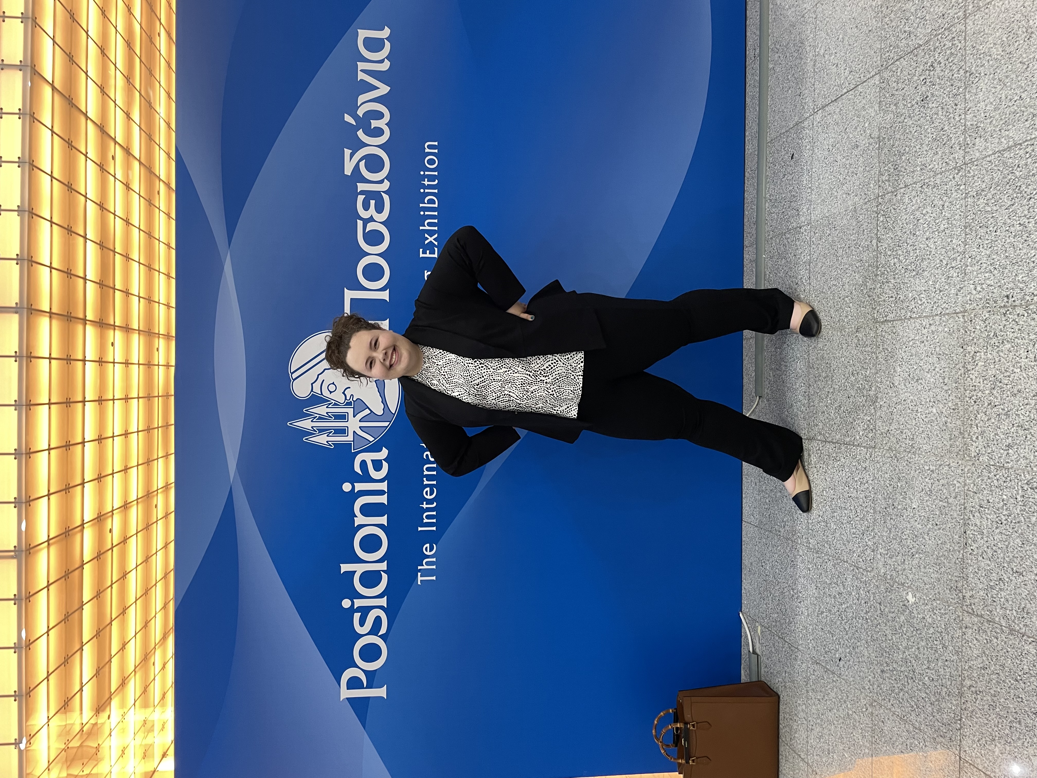 Samantha Weckesser ’23 M.Eng. ’24 smiles in front of the sign for the Posidonia Conference in Greece she attended in 2024.