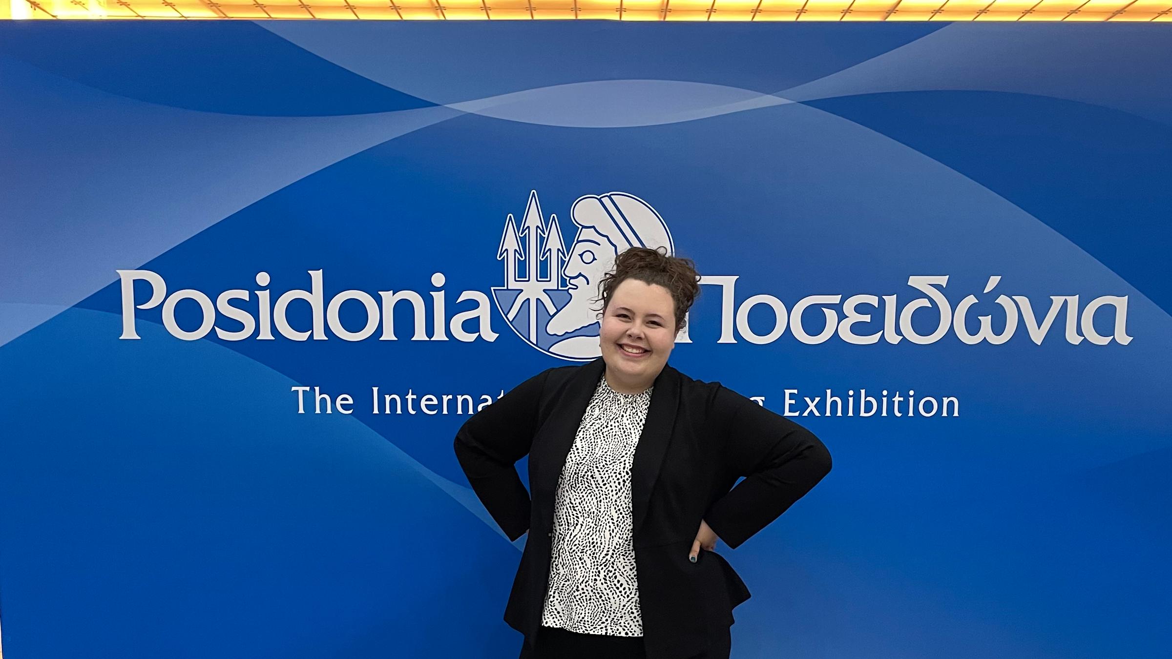 Samantha Weckesser ’23 M.Eng. ’24 smiles in front of the sign for the Posidonia Conference in Greece she attended in 2024.