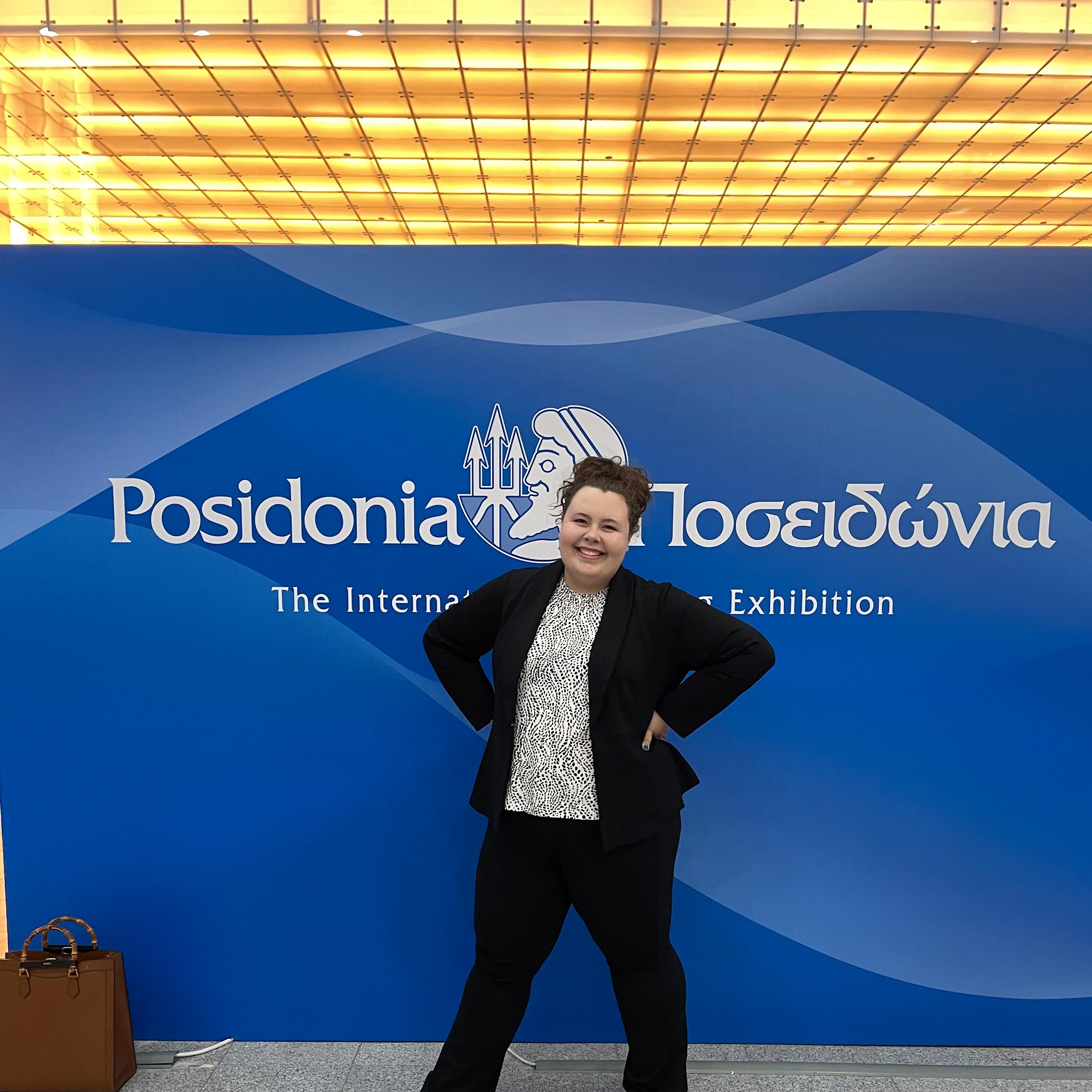 Samantha Weckesser ’23 M.Eng. ’24 smiles in front of the sign for the Posidonia Conference in Greece she attended in 2024.