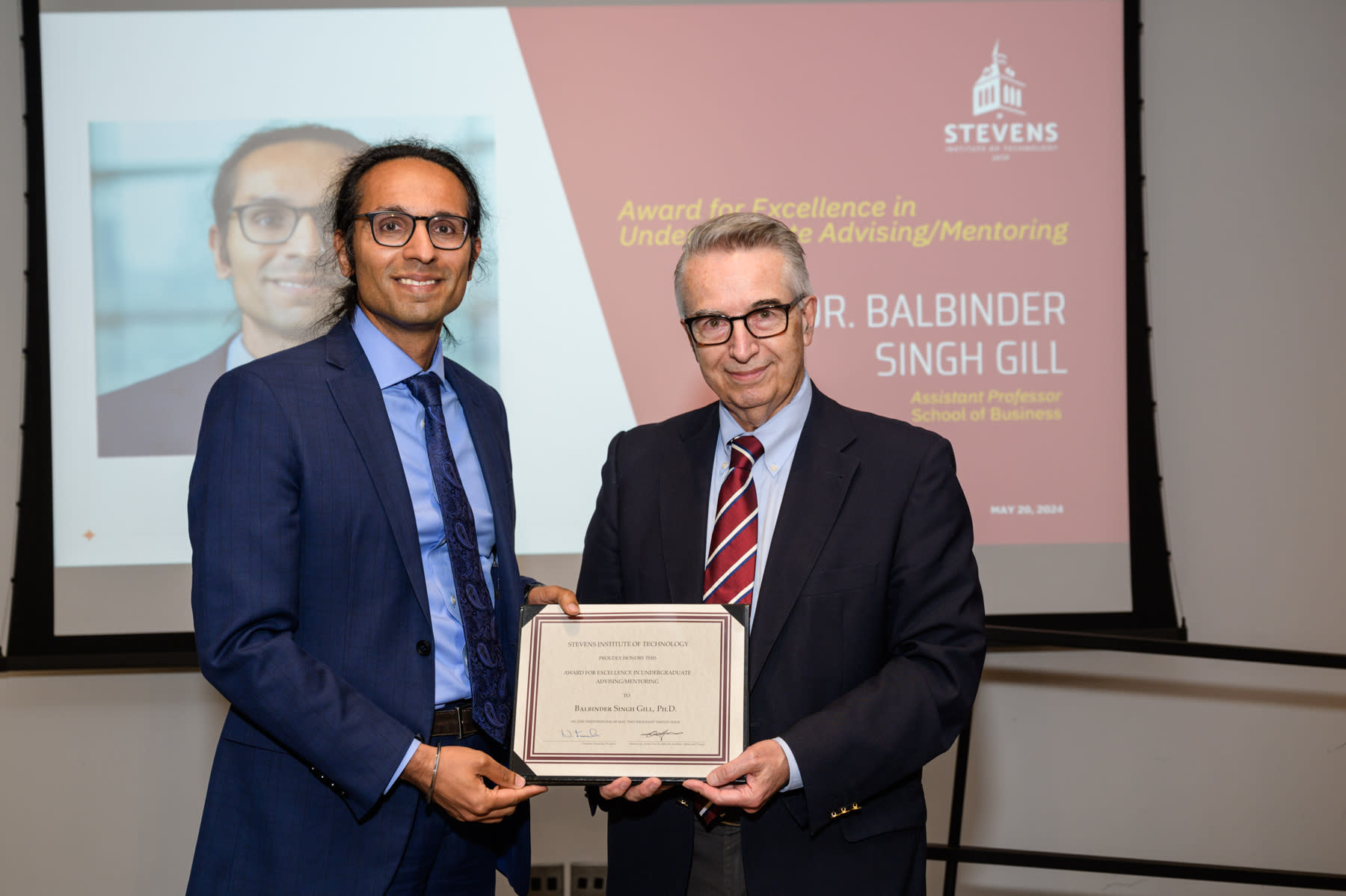 Balbinder Singh-Gill and Gregory Prastacos stand on stage holding the award certificate.